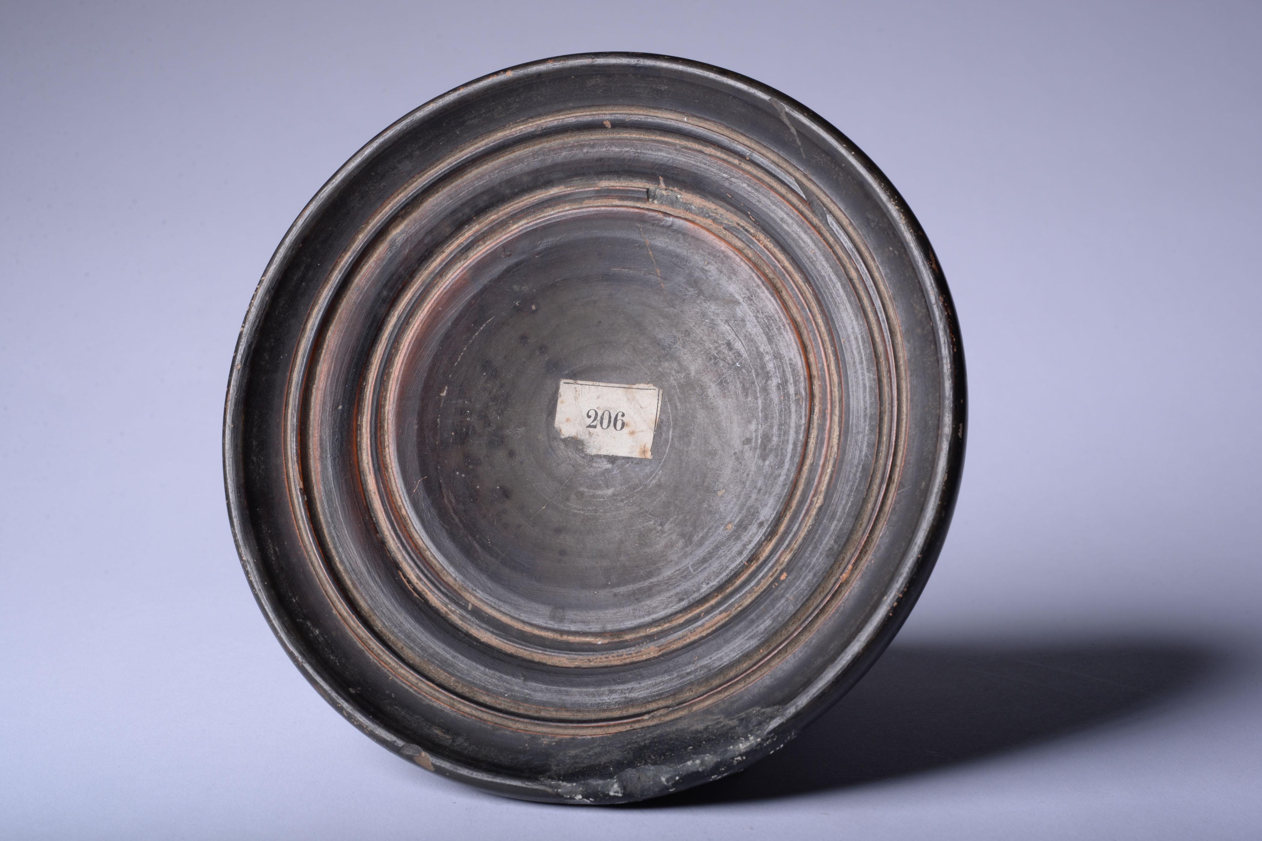 Ancient Greek black glaze terracotta dish 
South Italy
circa 4th century B.C.

A pleasing Greek black-glaze dish, with deep concentric grooves around the base, mirrored on the surface with delicate red ochre concentric rings. The piece is a fine
