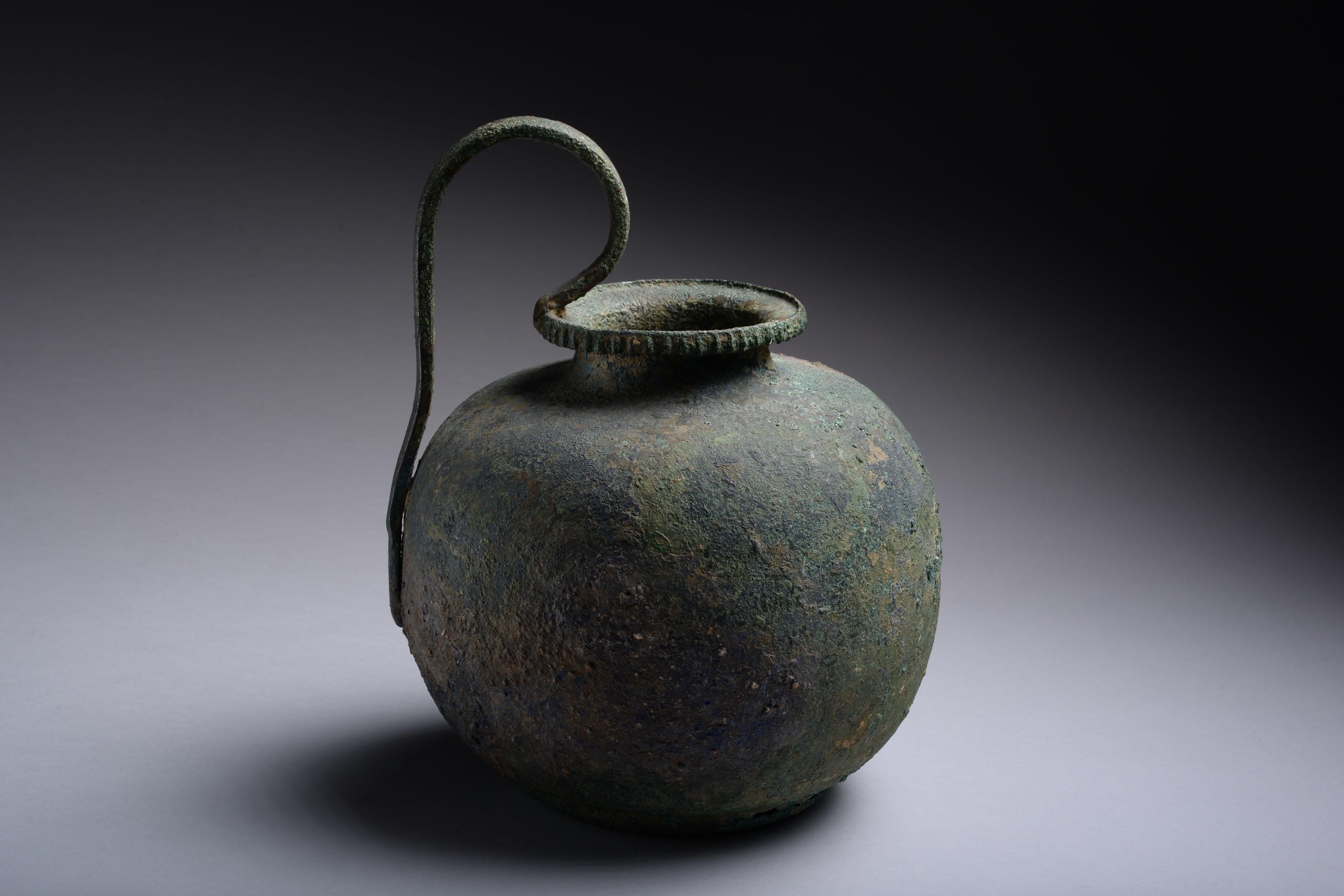 Large Greek bronze olpe vessel, used for pouring wine, dating to the 5th century BC. 

The rounded body with curved shoulders, narrow neck and everted rim with ribbed border. A separately made, elegant, tall handle curves from the lip to the