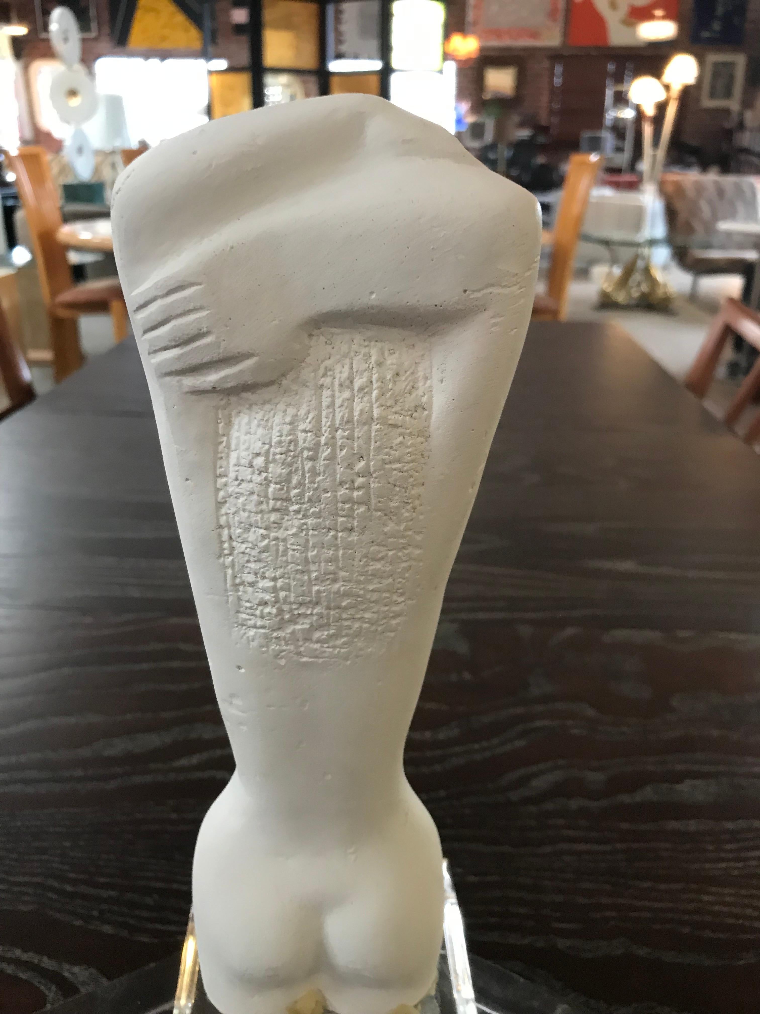 Small white plaster statue of a nude female. Rendered in a Primitive style similar to those of ancient Greek statuary from the early period; our statue has the same plated hair and 