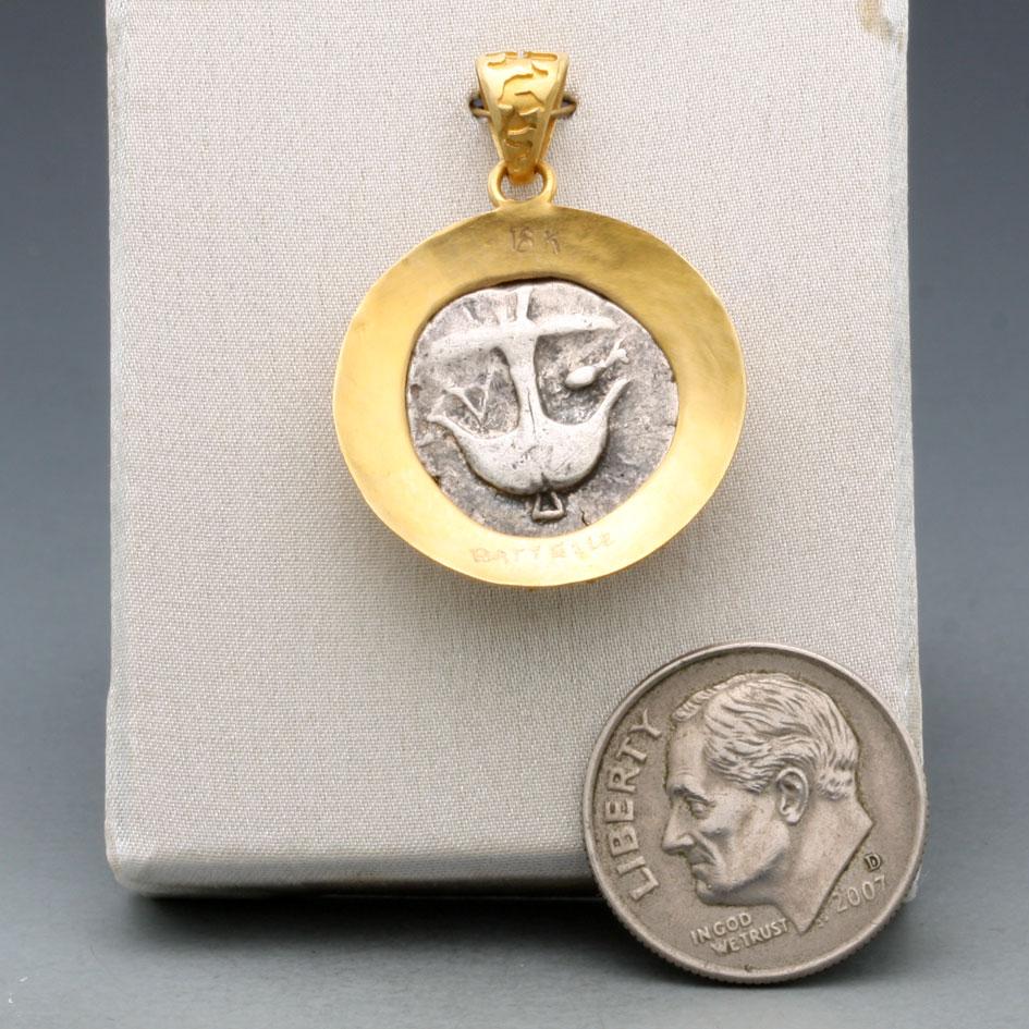 An authentic ancient Greek Coin from 450-400 BC featuring the face of Medusa with her protruding tongue and crown of snakes is surrounded with an intricate saw work bezel in 18K gold with a beautiful complementary effect.   Apollonia Pontica (on the