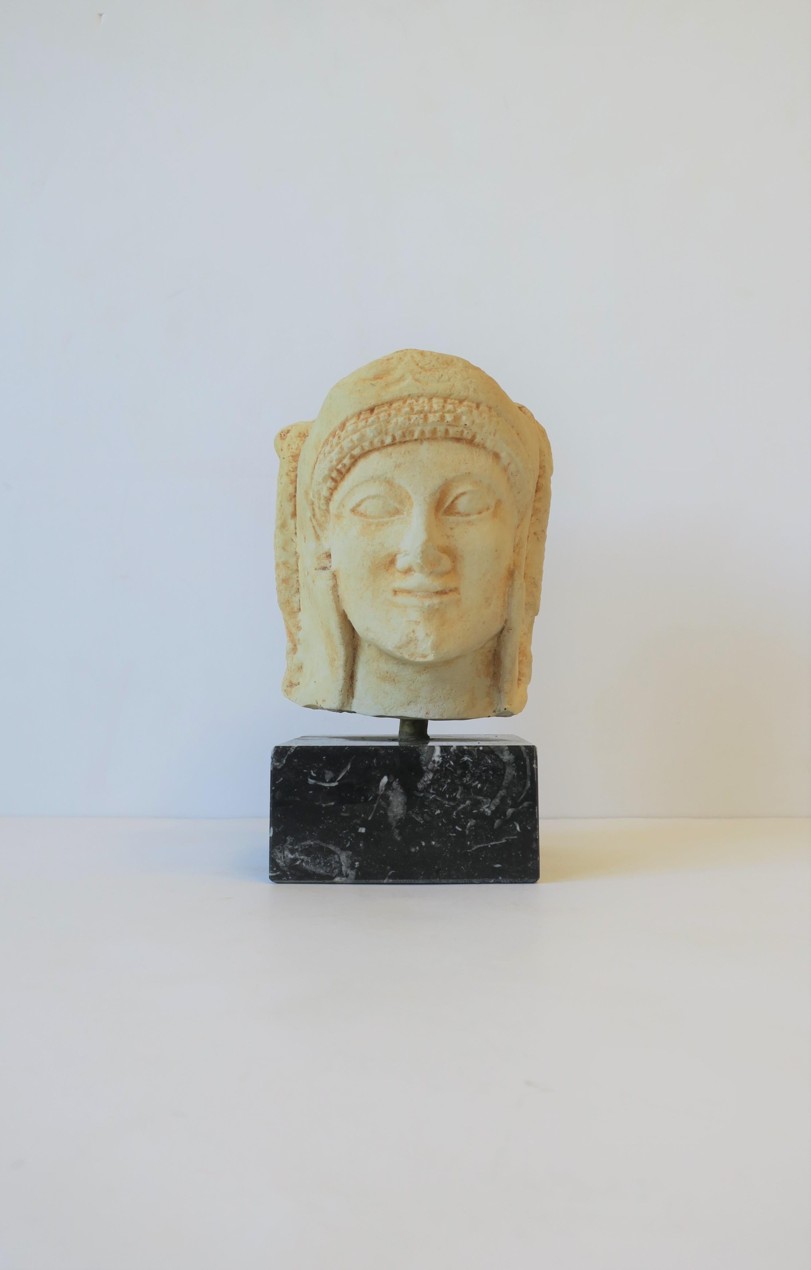 A substantial head/bust sculpture piece; a reproduction of the prehistoric Ancient Greek and Roman art period, circa 20th century, Greece. Piece is a matte resin (feels like stone) attached on a black and white marble base. 

Piece measures:
Overall