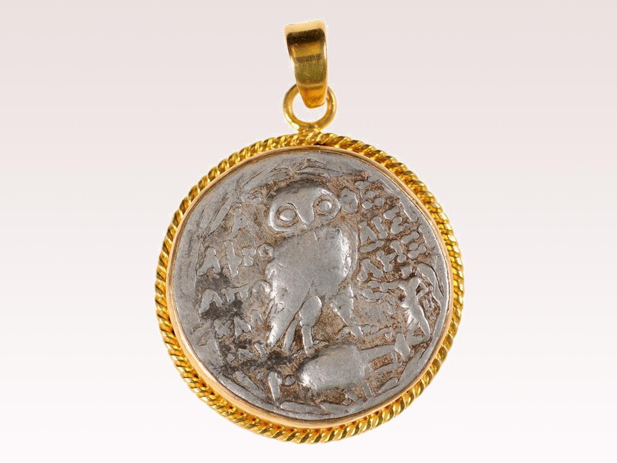 An authentic Greek, Attica, Athens AR Tetradrachm Owl coin (new style, circa 133-132 BC), set in a round, roped edge 22k gold bezel with 22k gold bail. The obverse, or front side of this coin features the head of Athena, wearing a crested Attica