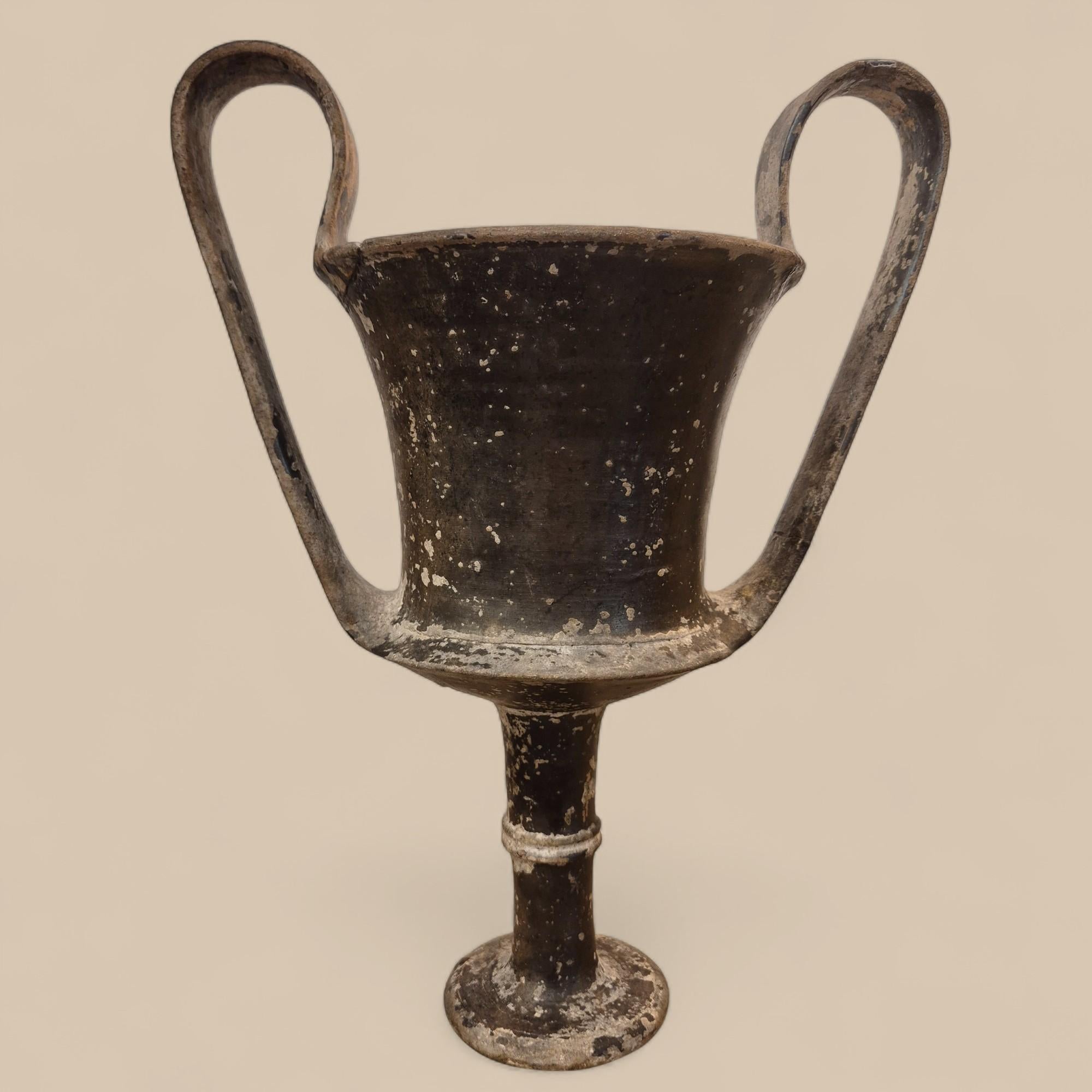 Questo elegante kantharos in terracotta, che si distingue per l'alto stelo e i doppi manici graziosamente arcuati, risale a circa 2000 anni fa, come confermato dall'analisi di termoluminescenza condotta dal Laboratorio d'Arte di Bruxelles