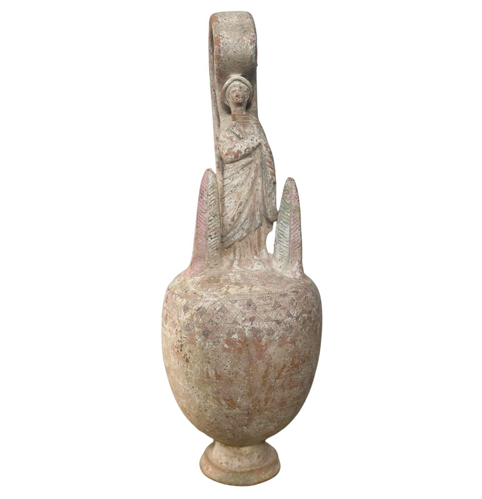 Ancient Greek Canosan terracotta votive vessel made in the c. 4th Century (B.C.). It consists of a tapered bulbous body with a human figure on top wearing a draped garment. The figure is flanked by two leaf figures on each side.
*Information on