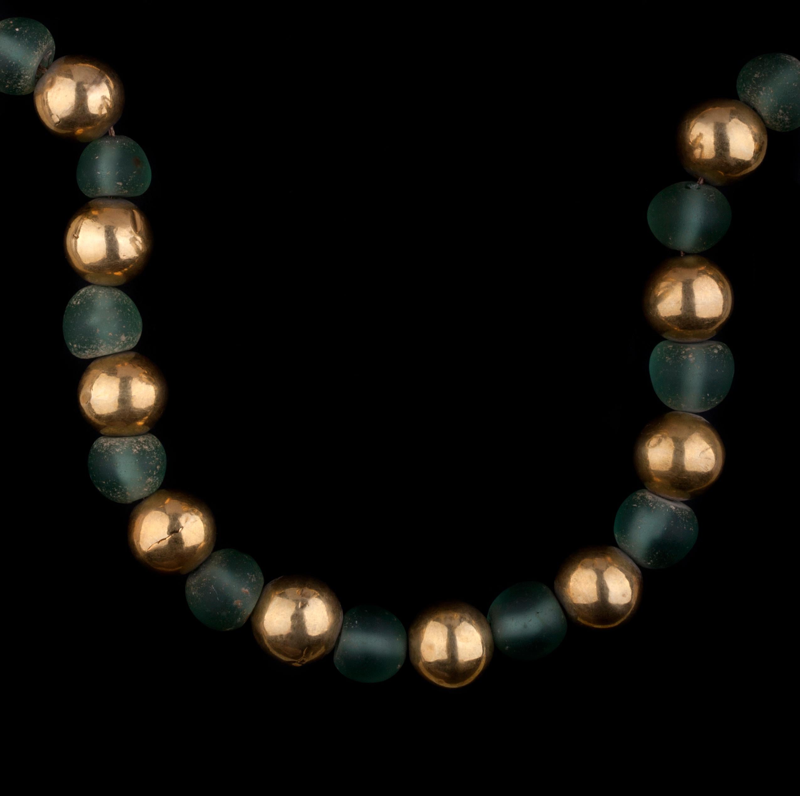 Un remarquable collier composé de perles anciennes en verre vert et en or jaune provenant d'une découverte archéologique.