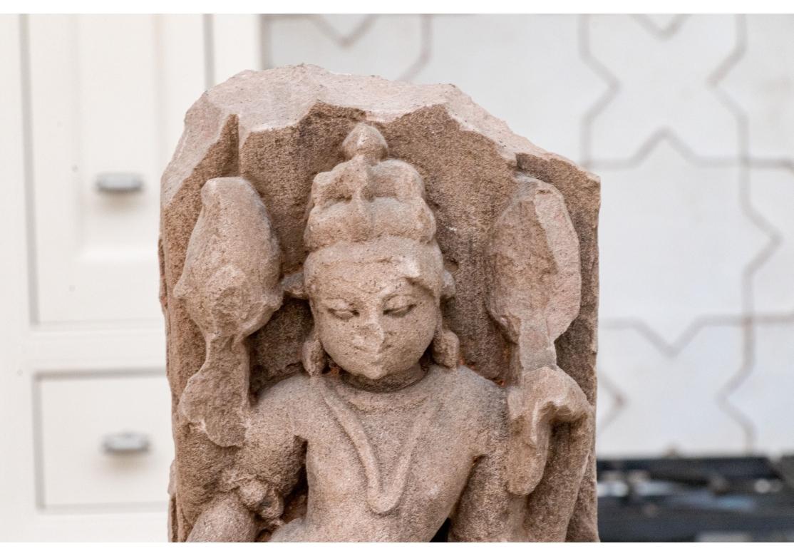 A likely 12-14th Century Northern Indian temple fragment of a female figure or consort known as an Apsaras. Carved in Red Sandstone, the female figure is appropriately attired in belt, girdle, necklace and bracelets and stands sensuously with one