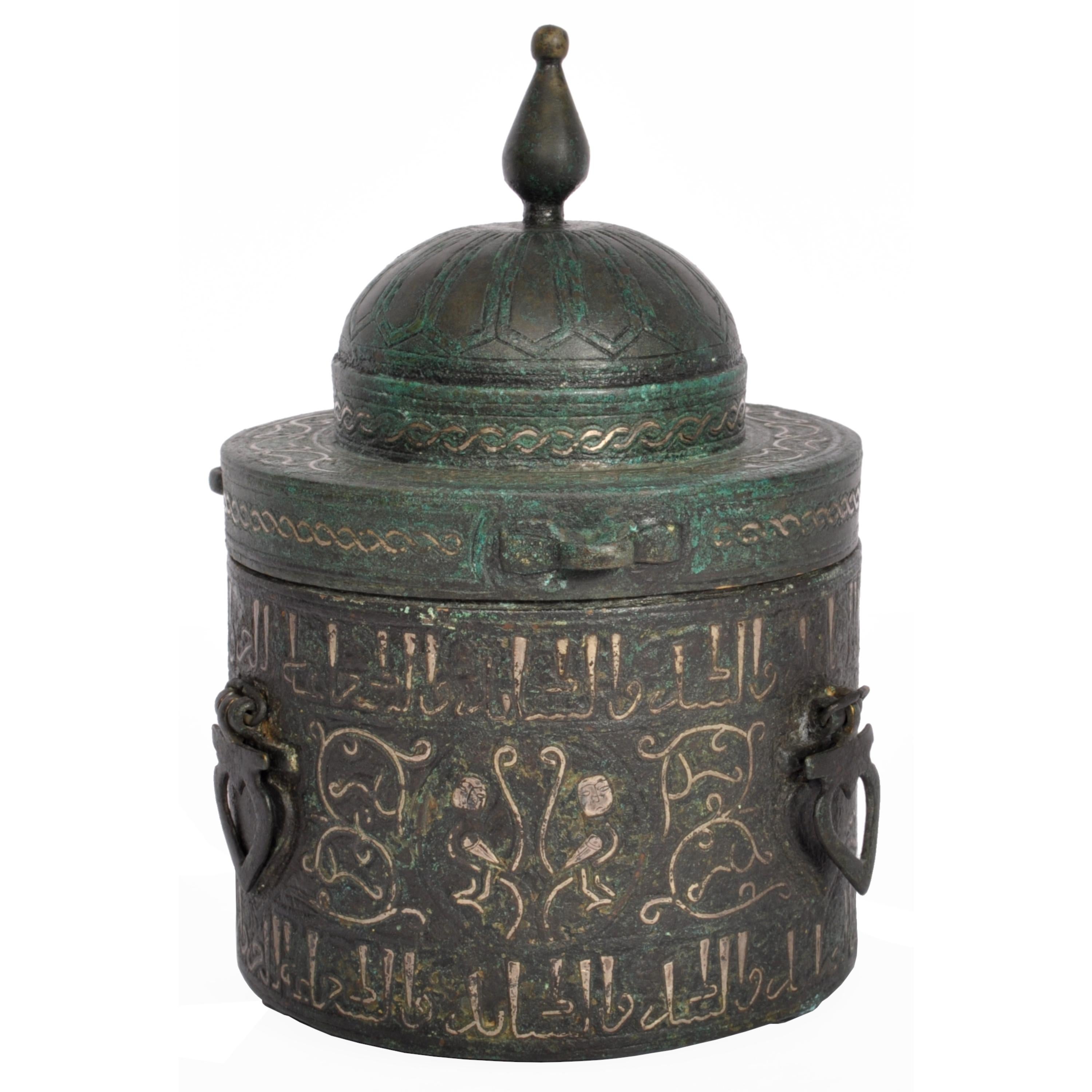 An important Islamic Khurasan bronze and silver-inlaid inkwell & cover, Eastern Persia, Circa 1200.
The inkwell of cylindrical form and having a shallow dome top cover with a tall knopped finial and inlaid with a twin band of scrolled silver. The