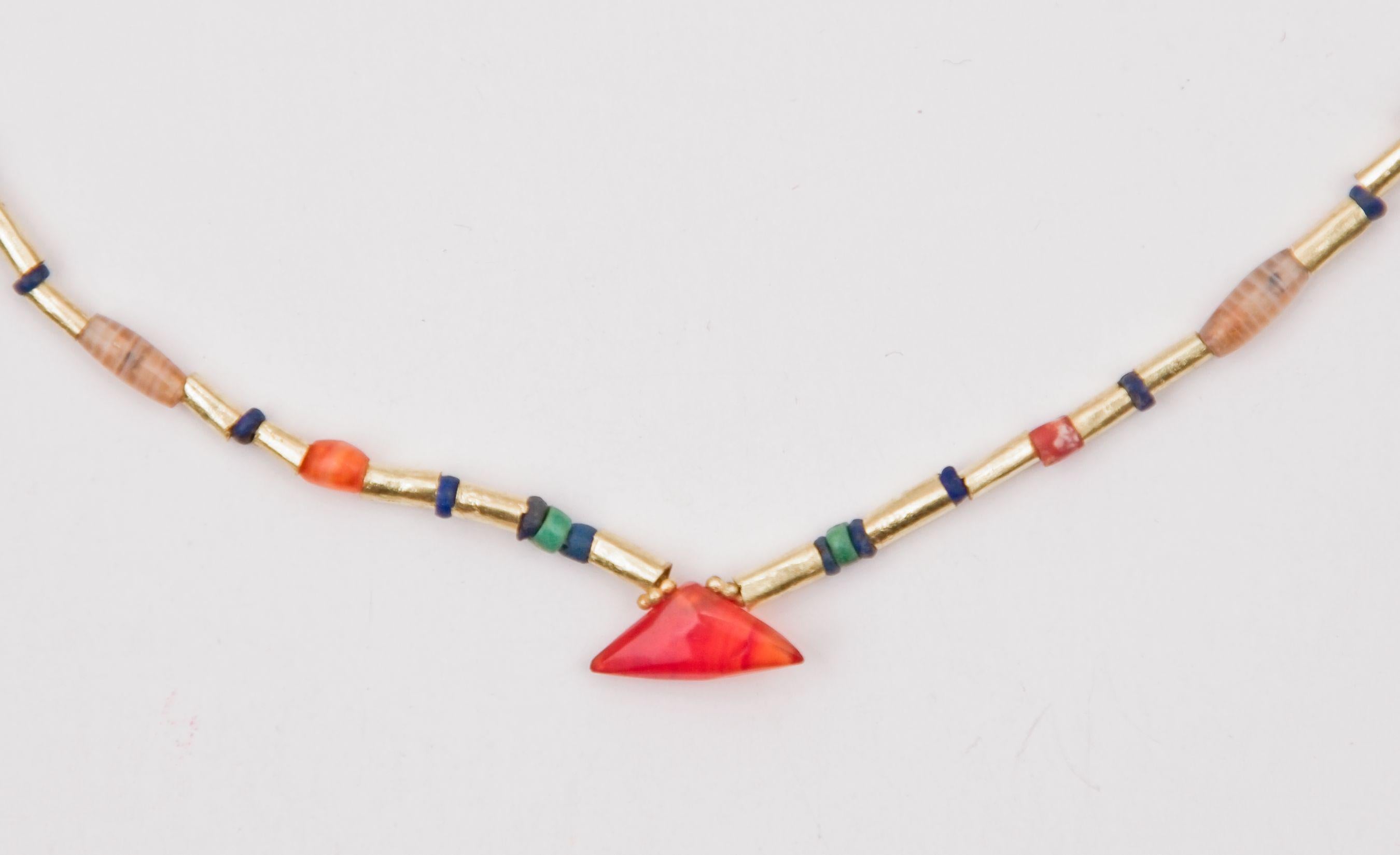 Very small agate, carnelian, turquoise, and lapis lazuli beads, alternating with seventy 22k gold cylinder beads with a triangular carnelian bead pendant at the center of the necklace. The pendant is 1.2 cm at the base of the triangle, 5.5 mm in