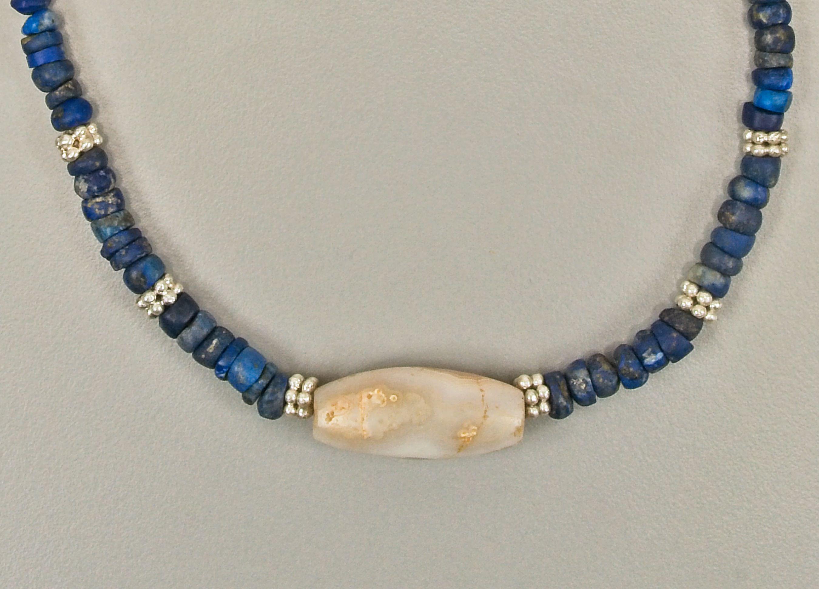Ninety lapis lazuli beads, with a white milky quartz barrel shaped bead at the center. The center bead is faced with two silver beads made of two layers of six grains in a hexagonal pattern. There are ten more of these beads evenly spaced throughout