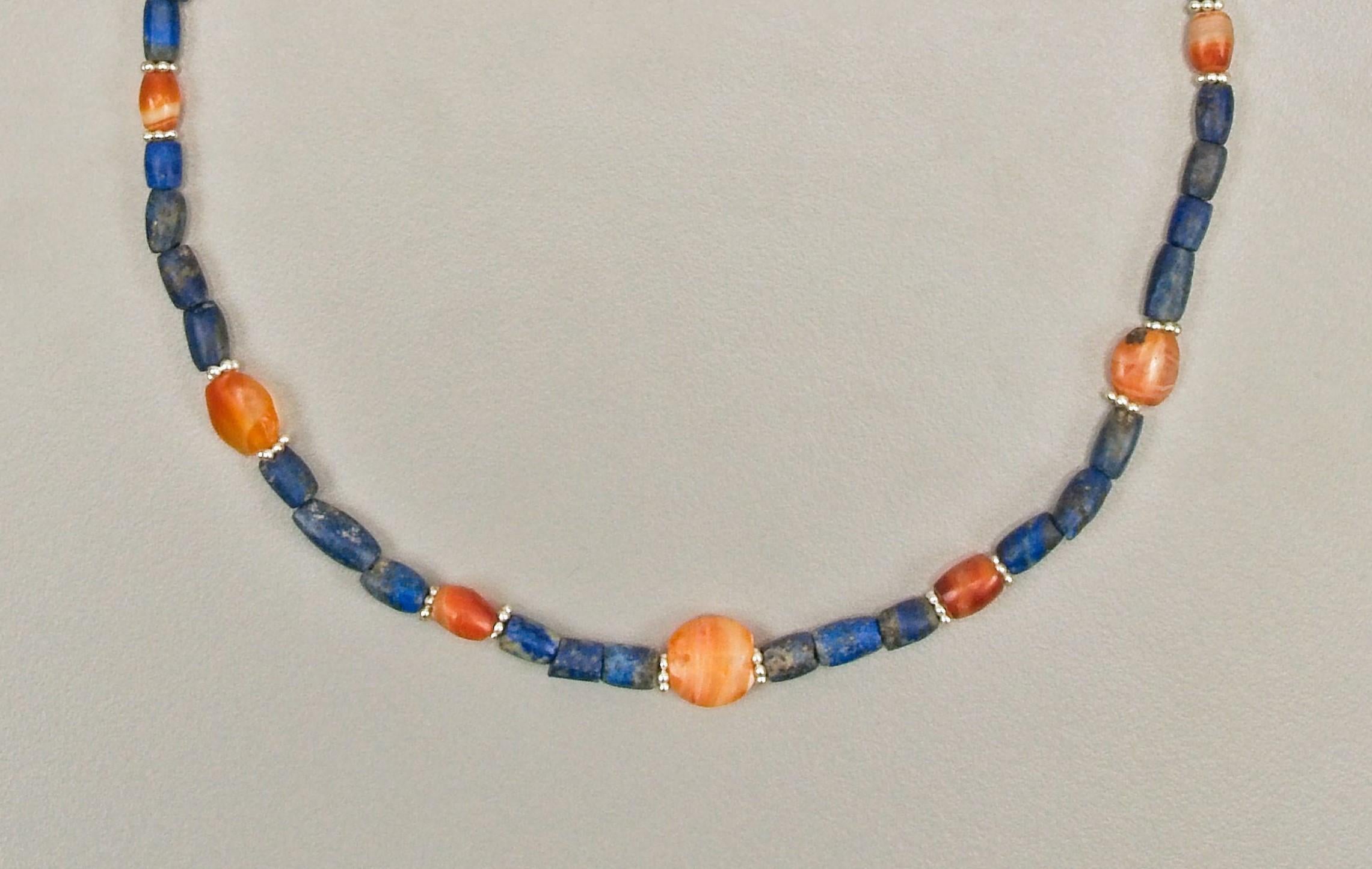 Forty-five barrel shaped lapis lazuli beads with nine carnelian beads, each faced with a granulated silver ring bead. Three of the nine carnelian beads are tabular, the remaining six are short barrel shaped beads. The center bead is 1.15 cm in