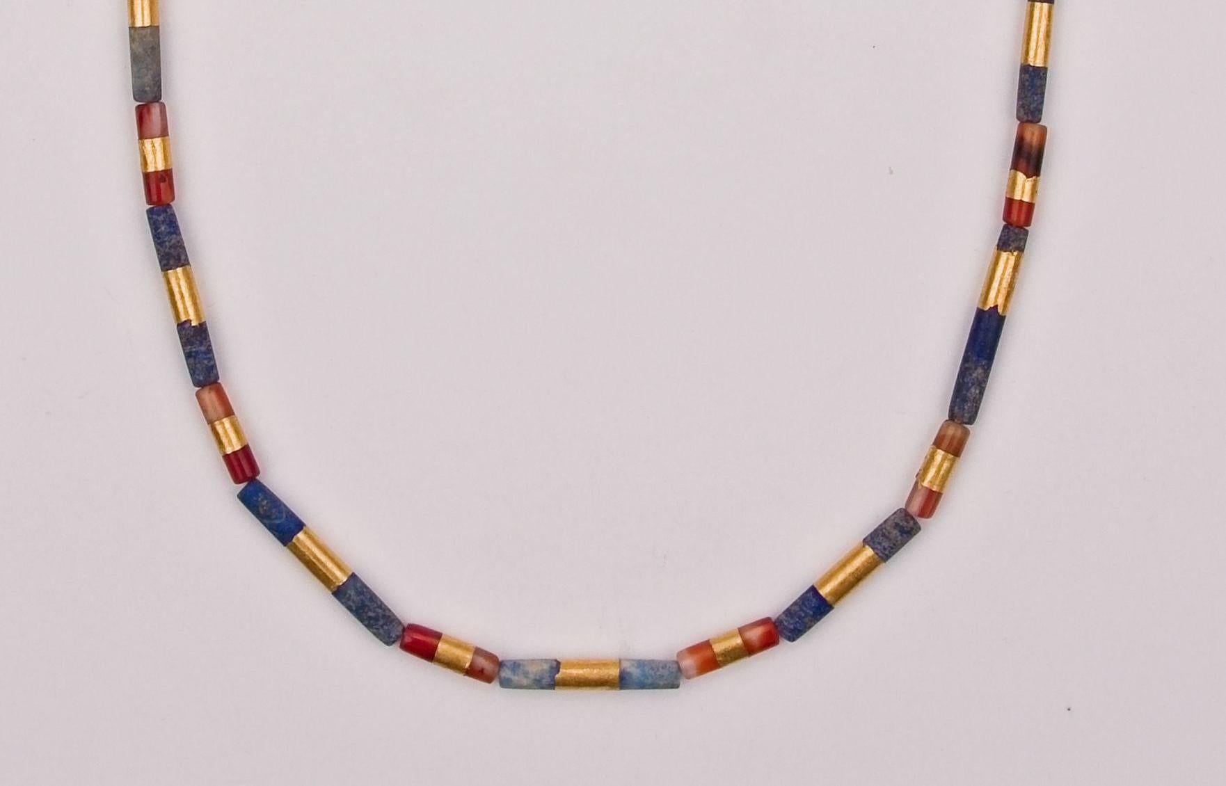 Fifteen long cylindrical lapis lazuli beads and fourteen somewhat shorter carnelian cylindrical beads alternating, all of which have a band of 22k gold encircling the bead at the center. The thin bands of gold cover about a third of the length at
