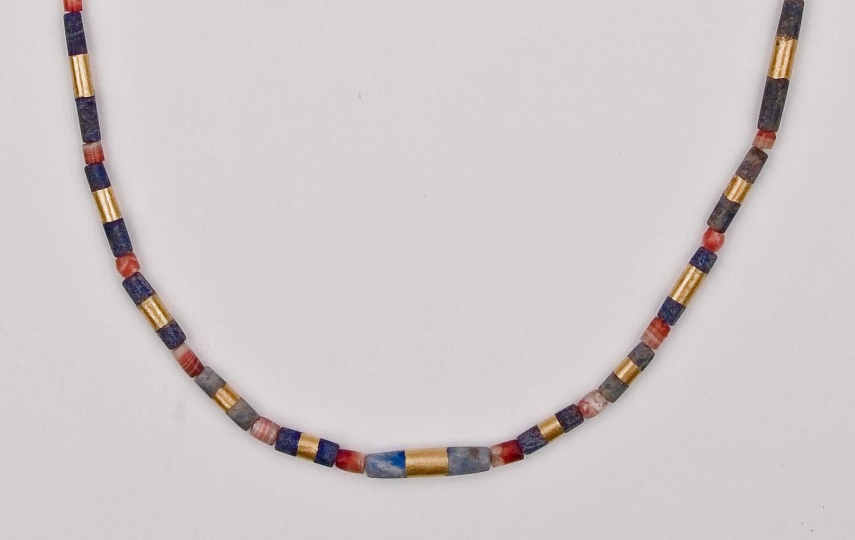 Twenty-six lapis lazuli cylindrical shaped beads, each with a band of 22k gold encircling it at the center, alternating with twenty-seven barrel-shaped carnelian beads. The lapis lazuli beads graduate in size towards the back of the necklace. The