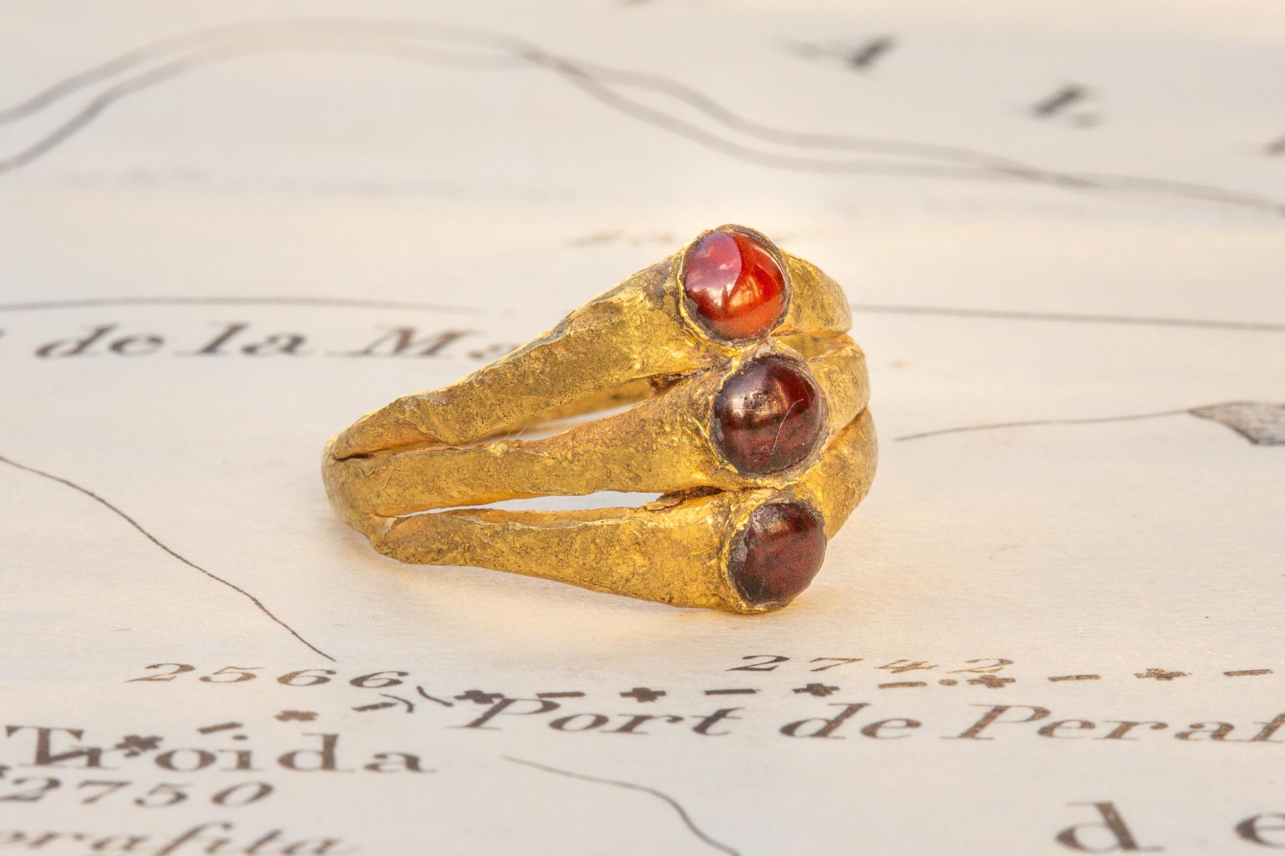 Ein schönes und seltenes Exemplar eines spätrömischen, dreilagigen Rings, besetzt mit Granatcabochons, um das 3. Das flache Band aus dickem, gehämmertem, hochkarätigem Gold gliedert sich an der Lünette in drei flache Goldbänder, die jeweils in der