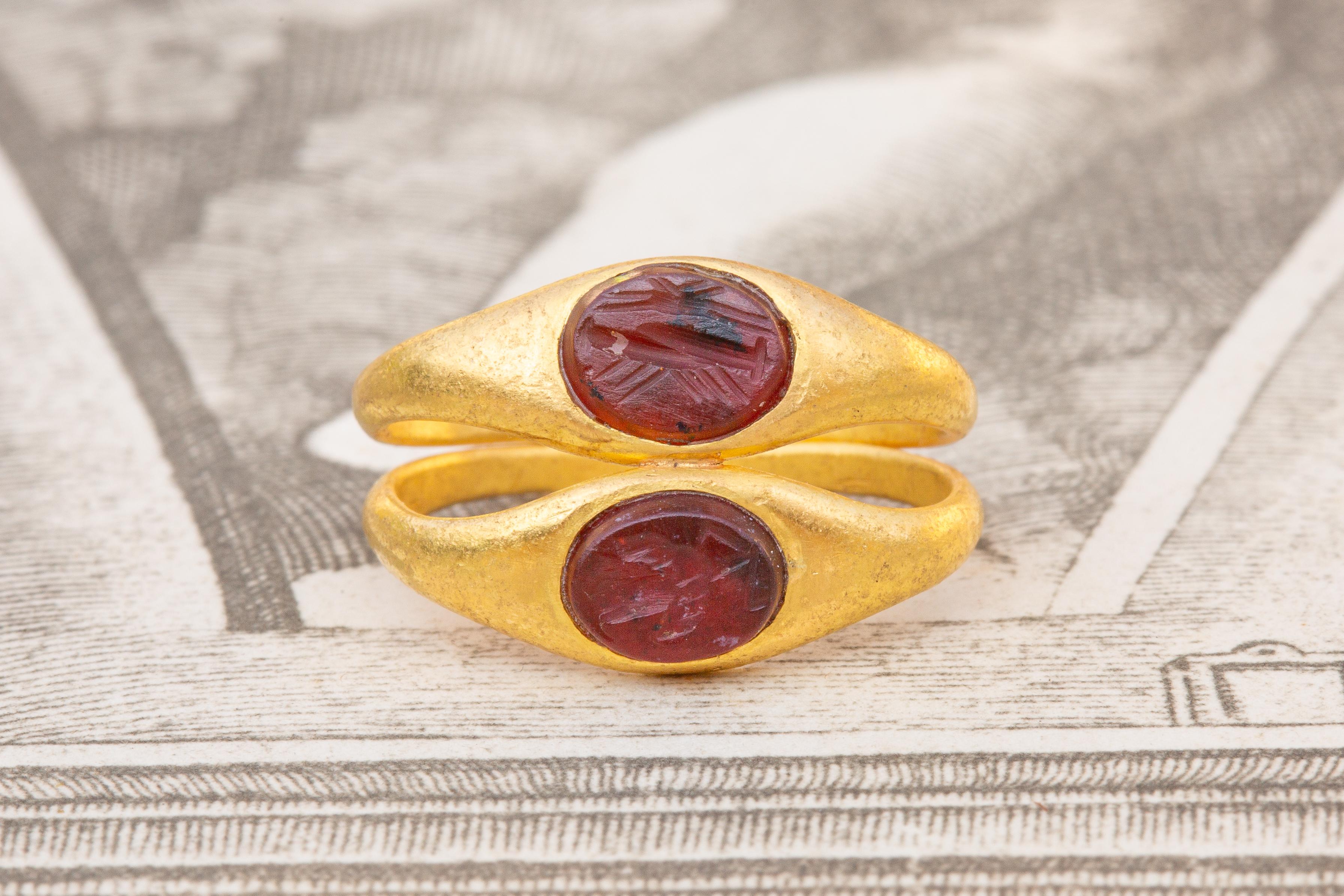 A beautiful and scarce example of an Ancient Roman ‘twin’ ring set with carnelian intaglios, circa 1st - 3rd century AD. The mount is crafted in high karat gold and bifurcates at the very back of the shank into twin bands which reconnect at the