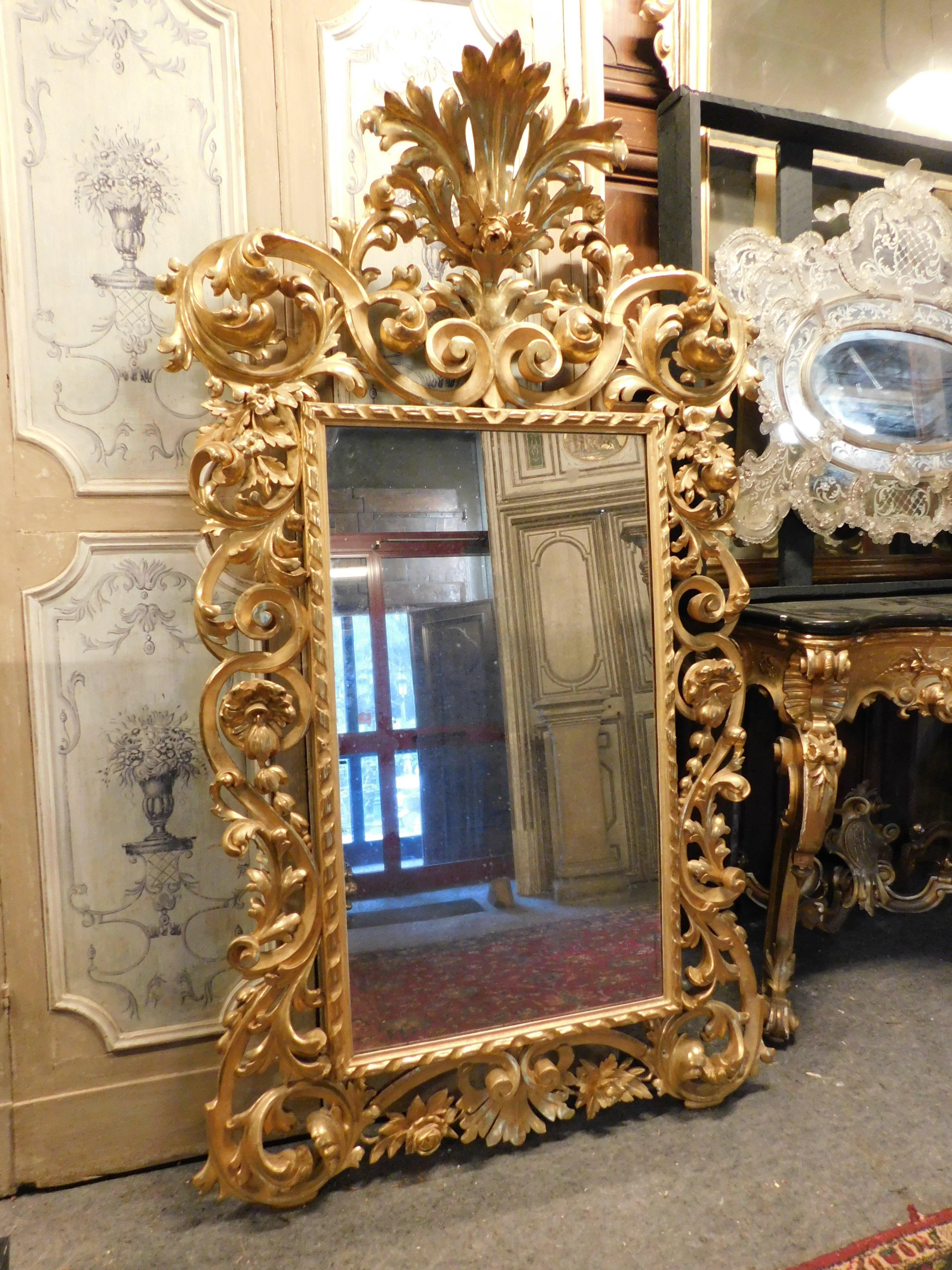 Ancient mirror in gilded wood, rich handmade fretwork decoration, with volutes and floral and leafy elements, large carved crown. Period 1800s, from southern Italy (Naples). Furnishing element of great charm and scenic presence. To enrich entrances