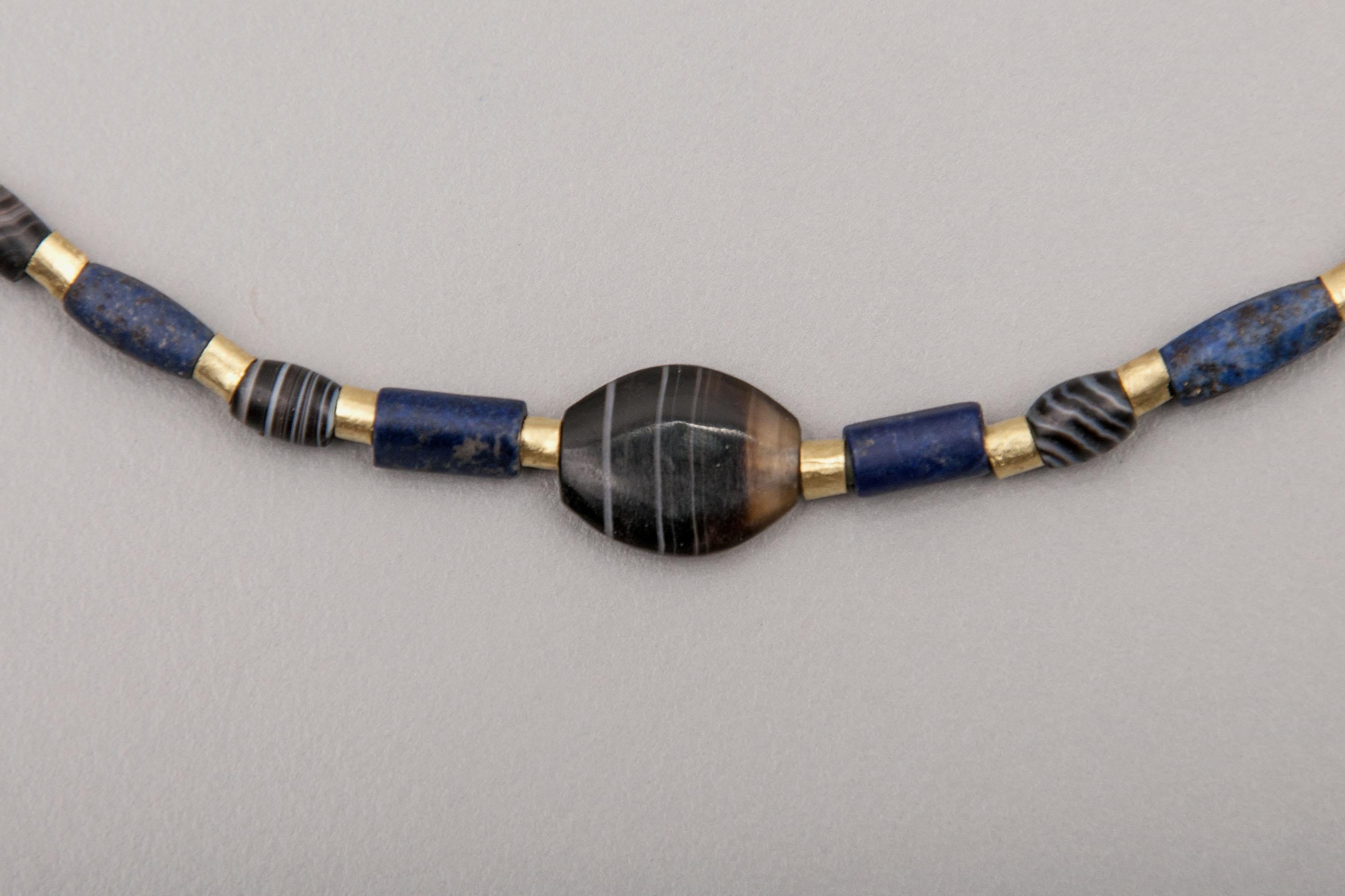 Twenty-six very small black onyx barrel beads alternating with twenty-eight lapis lazuli cylinder beads. Between each of the stone beads is a 22k gold tube bead. At the center of the necklace is an onyx lozenge shaped bead 1.15 cm in length, 9 mm in