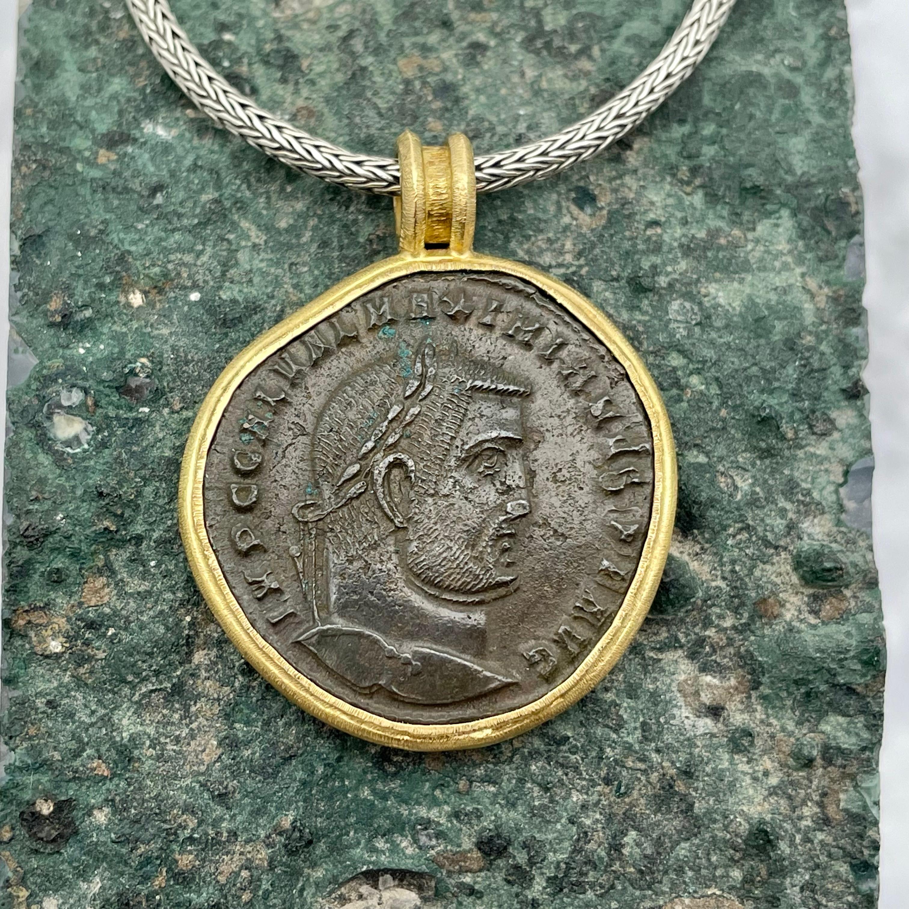 An authentic large bronze folis coin from 308 CE depicting the Roman Emperor Maximinus II in profile is set in a Steven Battelle designed 18K gold line texture handmade bezel below a simple double loop bail. Galerius Valerius Maximinus Daza, also