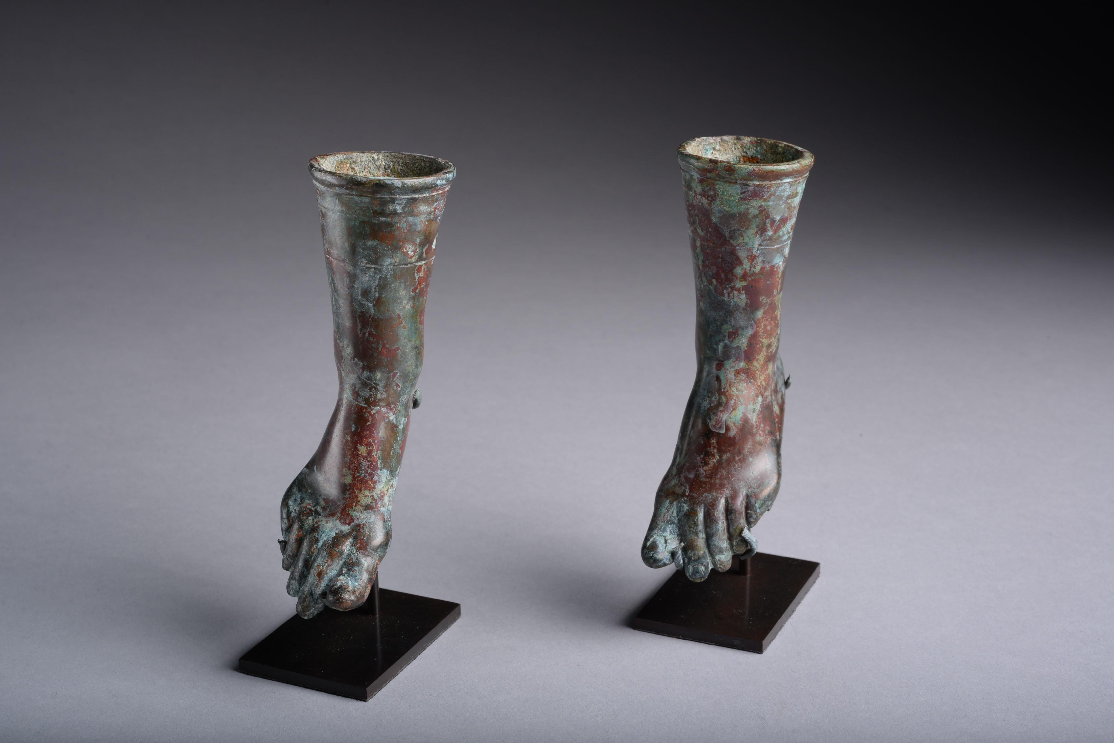 A pair of bronze fittings from a large Roman vessel or piece of furniture, dating to the 1st century AD.

In the form of bare human feet, finely modelled to show the nails and creases of skin, the big toes slightly raised.

Measures: Height 4
