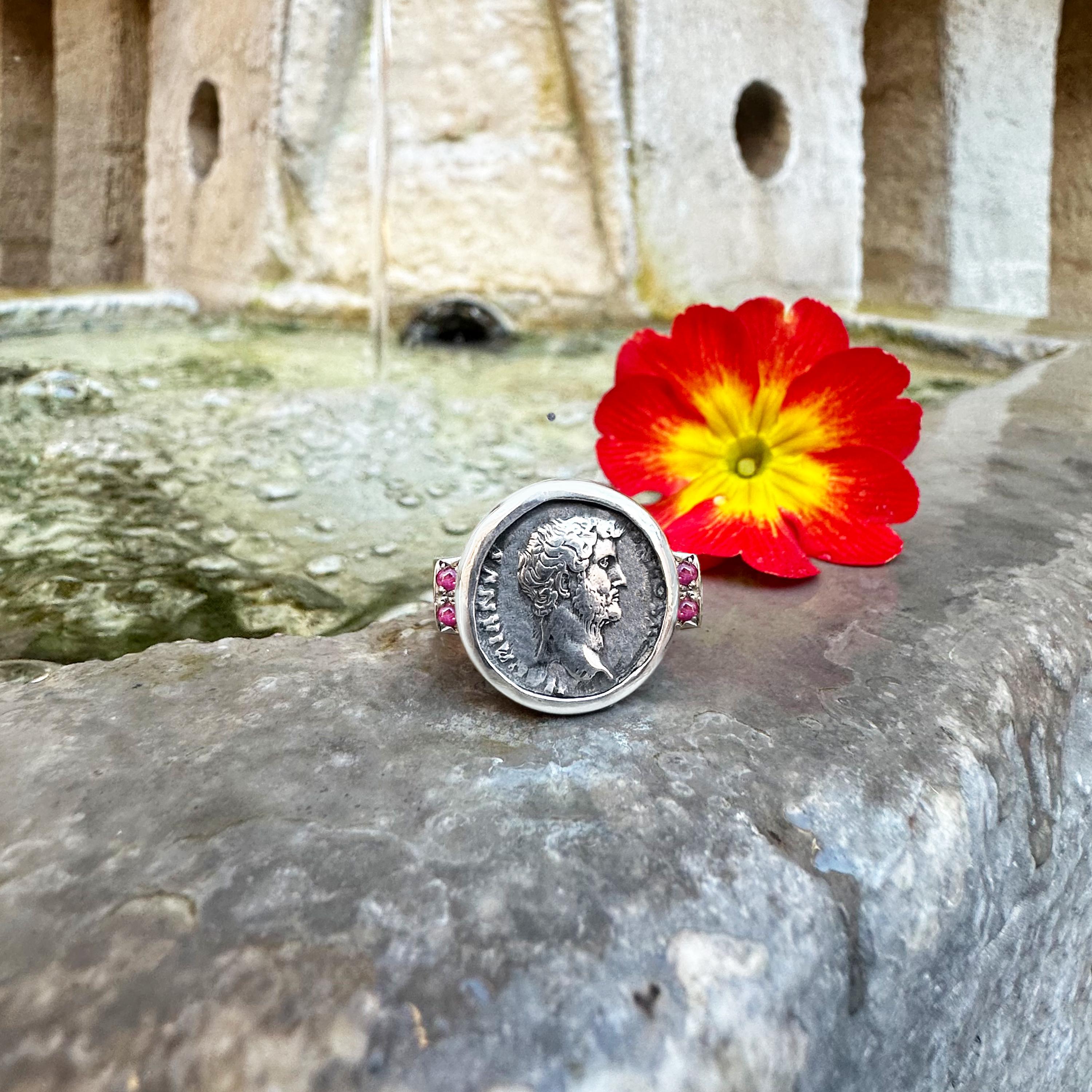 Contempla este exquisito anillo de plata de ley adornado con cuatro delicados rubíes. En su interior se esconde un verdadero tesoro: una auténtica moneda romana con la majestuosa efigie del emperador Adriano. Conocido por sus ilustres viajes, sus