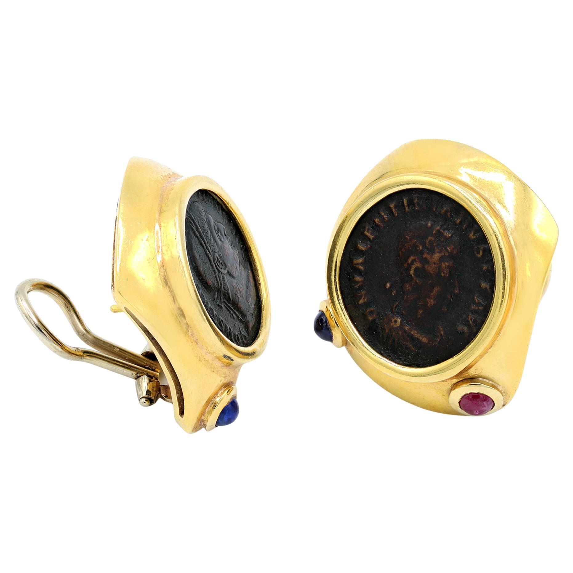 Une paire de boucles d'oreilles à clip vers 1960-70 représentant des pièces de monnaie romaines antiques. La monture est en or jaune 18 carats, ornée de petits saphirs et rubis cabochons sur la face inférieure de la lunette. Les quatre cabochons ont