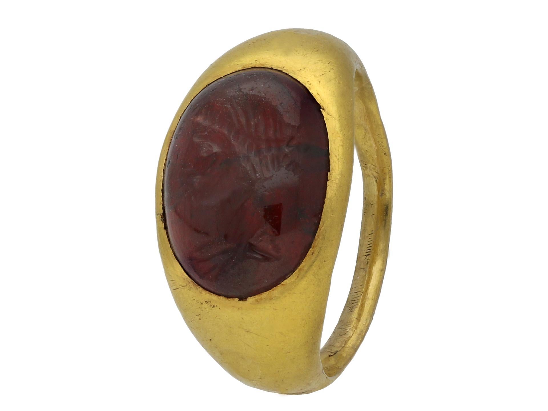 Ancient Roman female bust intaglio ring. Set horizontally to centre with an oval red glass cabochon intaglio in a closed back rubover setting, finely carved with a female bust, leading to heavy integrated shoulders and flowing through to a tapering