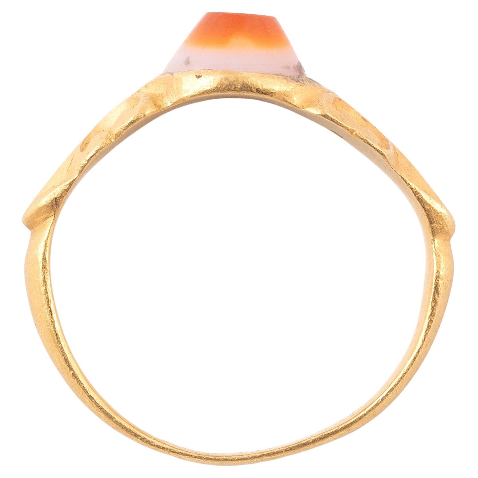 This is an ancient Roman gold intaglio ring dating to the 3rd century AD. This example is still set with the original intaglio in banded agate. The gem is set within an oval box-shaped bezel. The shoulders are delicately sculpted with raised design.
