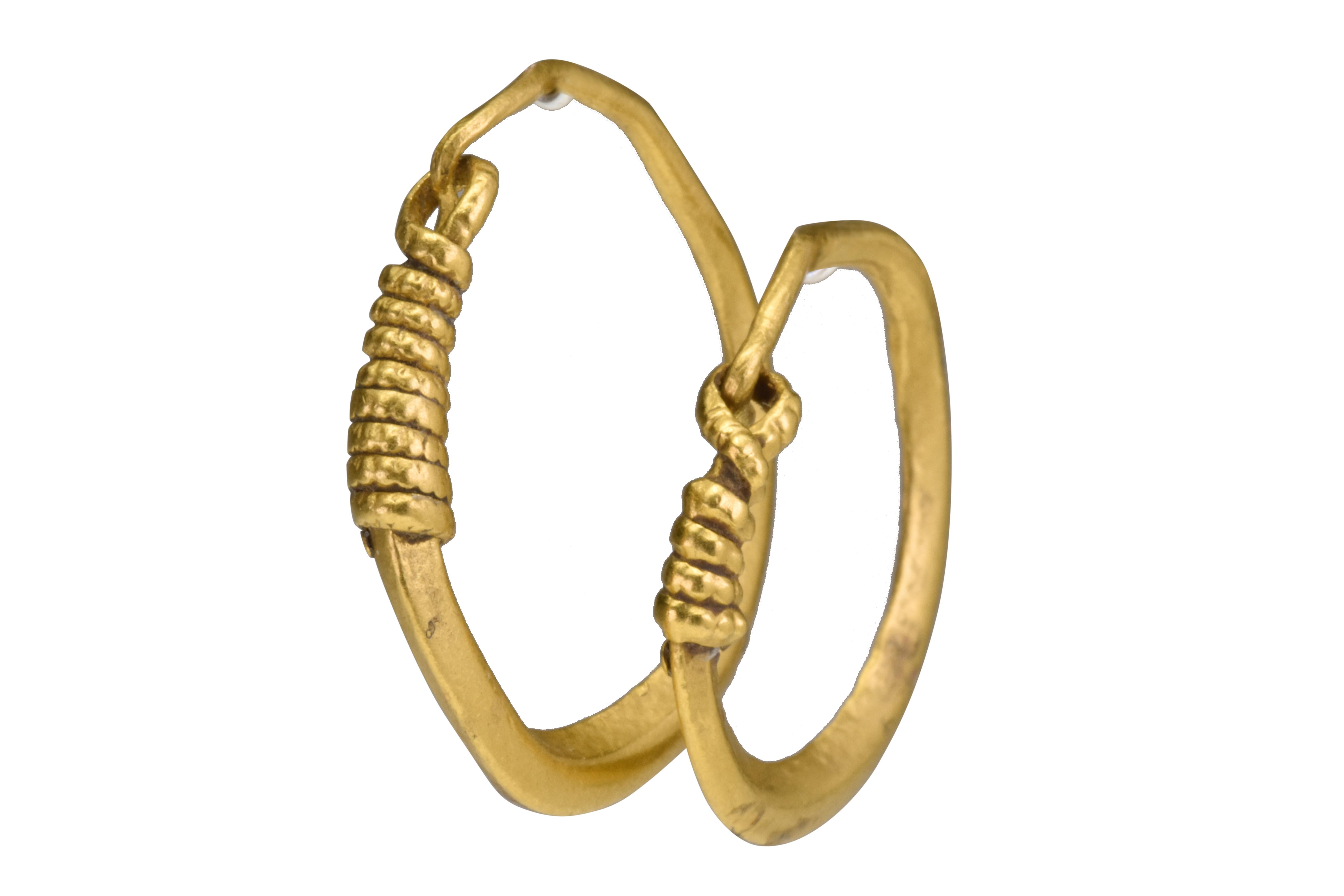 Ancient Roman Gold Earrings 

Ancient Roman, Ca. 200-300 AD

A matched pair of gold earrings, each of a thick round hoop with a carinated profile and tapering terminals ending with a hook. The opposite pair of terminals is embellished with coiled