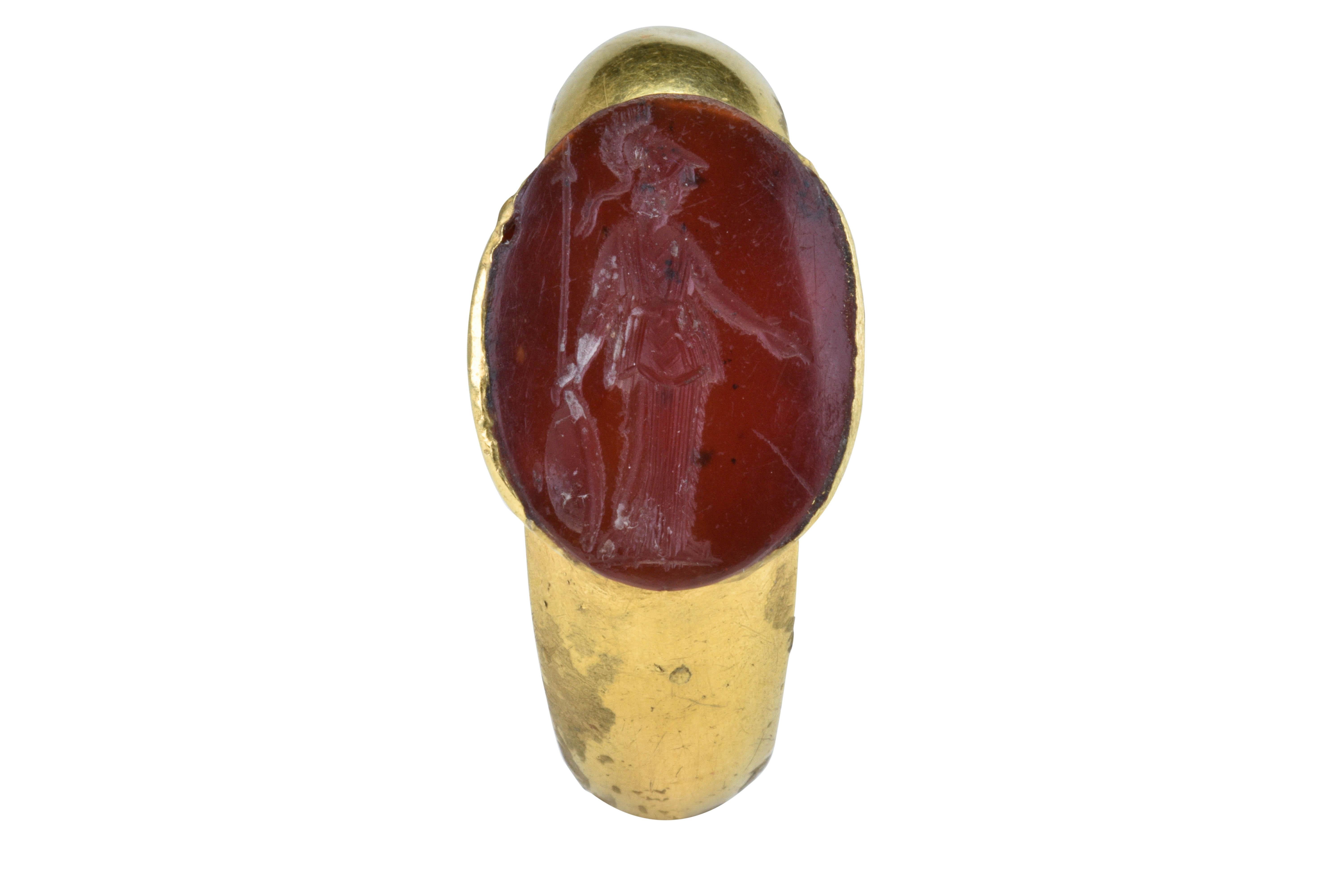 Ancient Roman Gold Intaglio Signet Ring with Standing Minerva

Ca. 100-300 AD

An Ancient Roman gold signet ring of a smooth, round band with applied bezel set with red hardstone intaglio engraved with a depiction of facing right, standing figure of