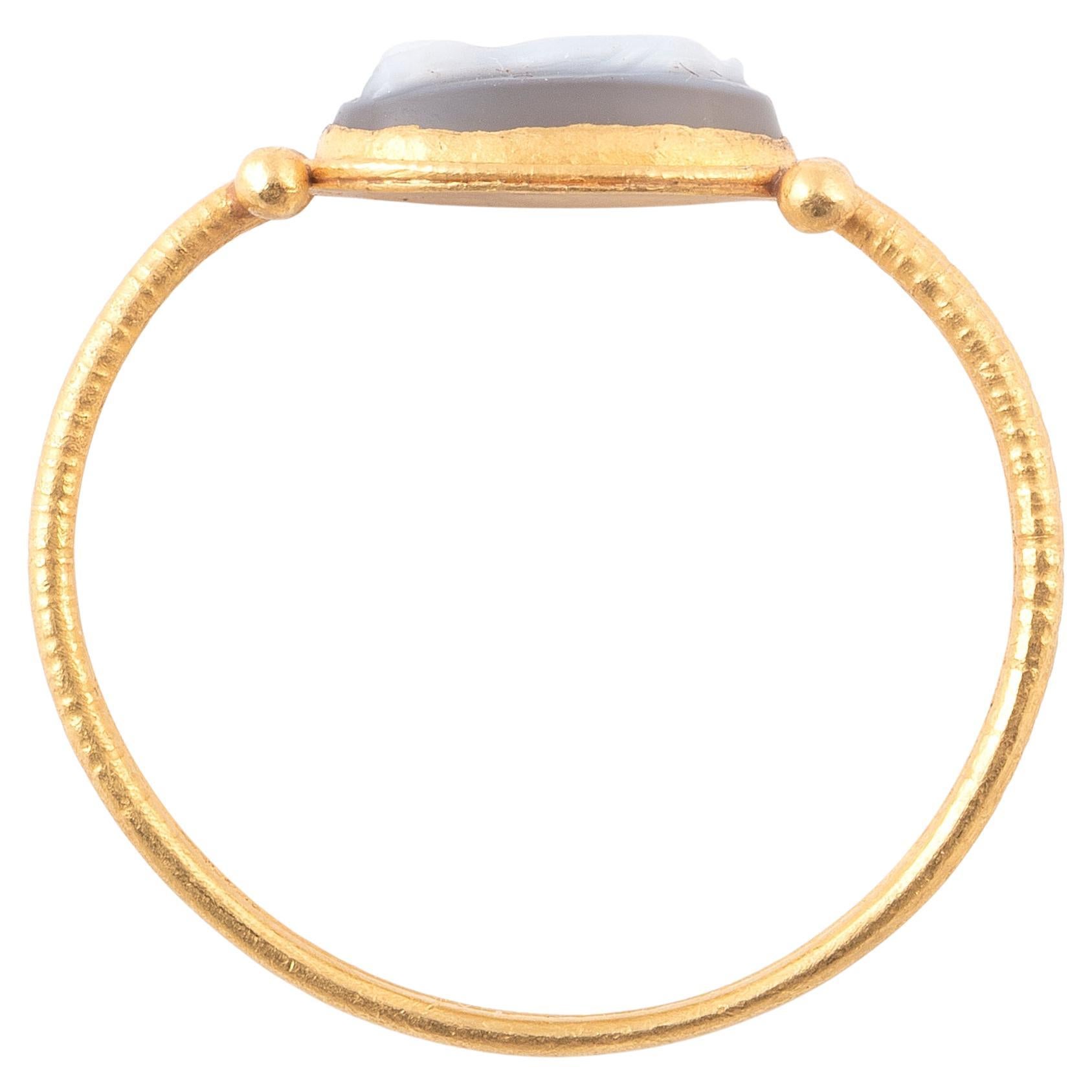 This delightful finger ring is in the style of the 2nd century A. D., with two distinctive pairs of gold globules soldered to the junctions of the round hoop and bezel. A agate cameo depicting the fish is inset in a circular bezel with a chased