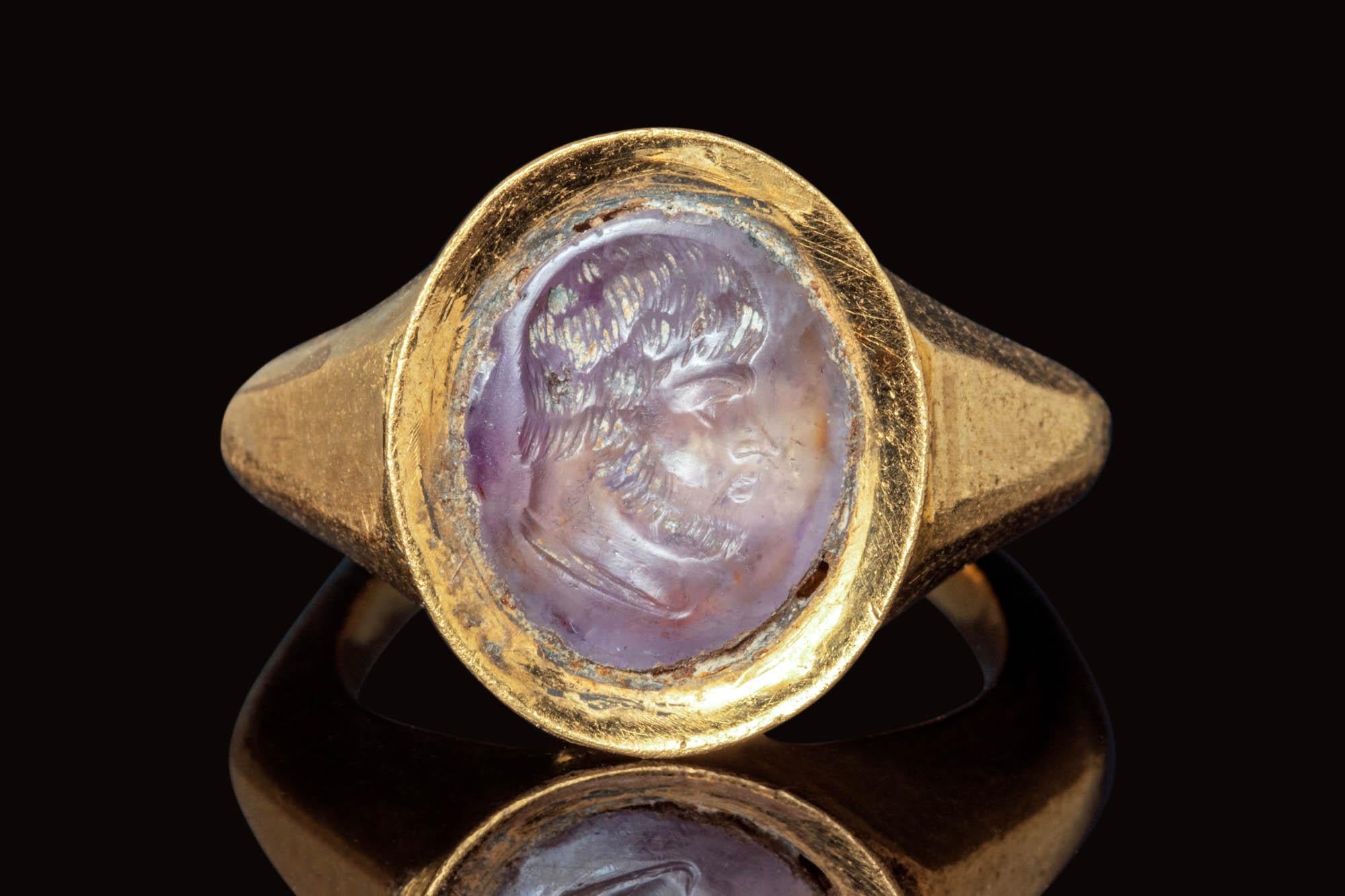 Anello romano in oro raffigurante un uomo barbuto rivolto verso destra. La figura è realizzata in modo naturalistico, con capelli corti e barba. An He ha un viso dettagliato con un naso lungo e dritto. L'anello ha un cerchio angolare che poggia su