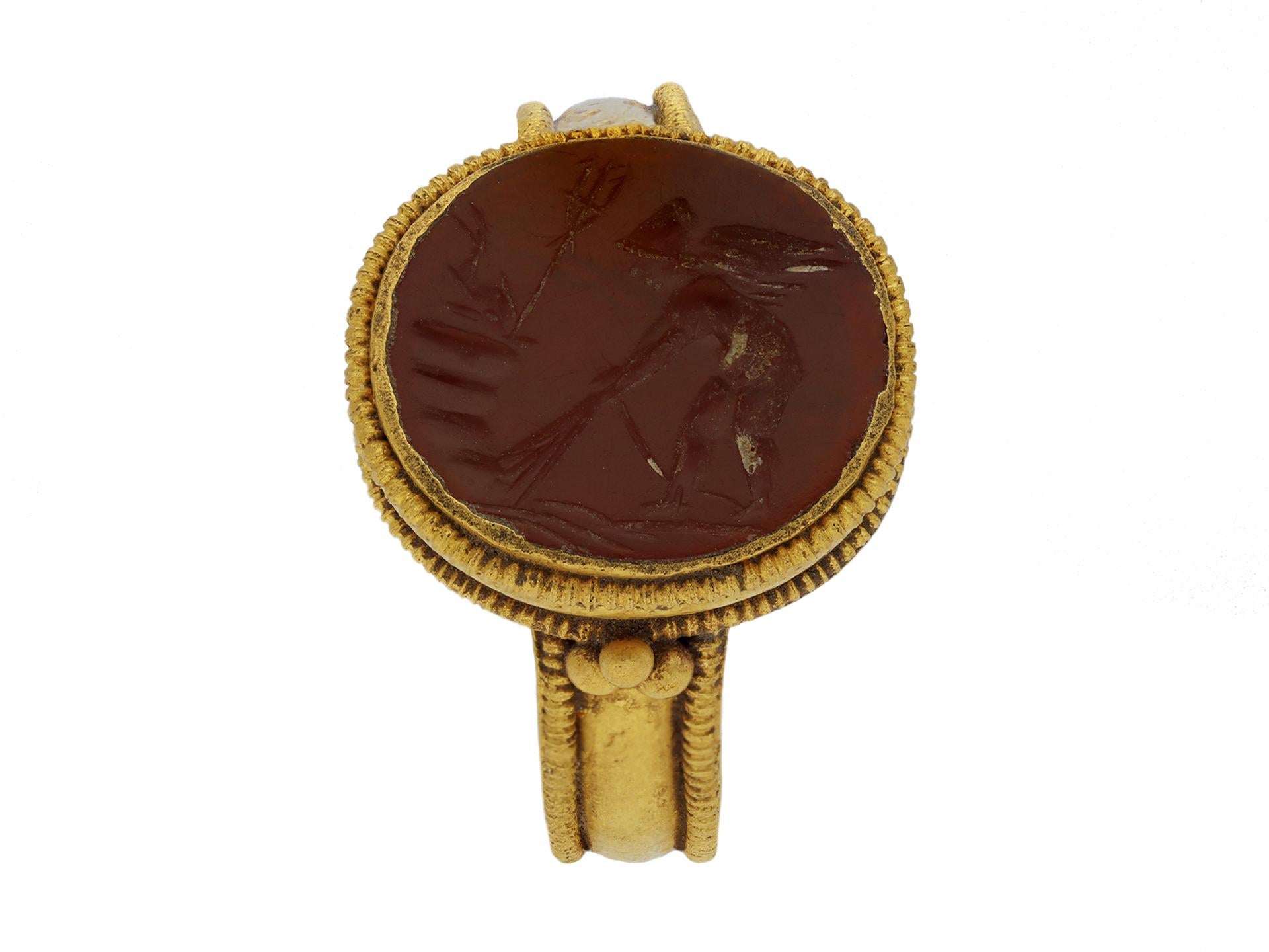 Ancient Roman gold ring with intaglio of Neptune. Set with an oval glass cloison intricate intaglio of a winged figure bowing to Neptune with trident and dolphin, in a closed back Roman set setting with a double border of granulation and flanked by