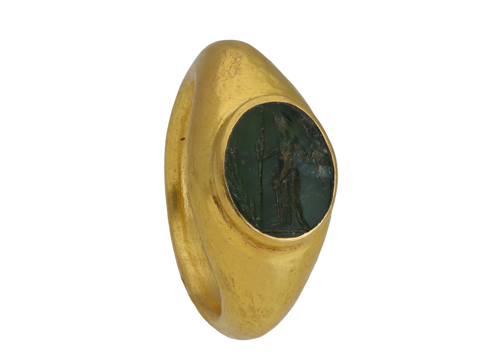 Ancient Roman gold ring with Minerva intaglio. Set to centre with an oval hardstone intaglio in a closed back roman set setting, finely engraved with an image of the goddess of wisdom and war, Minerva, who is depicted wearing a helmet and holding a