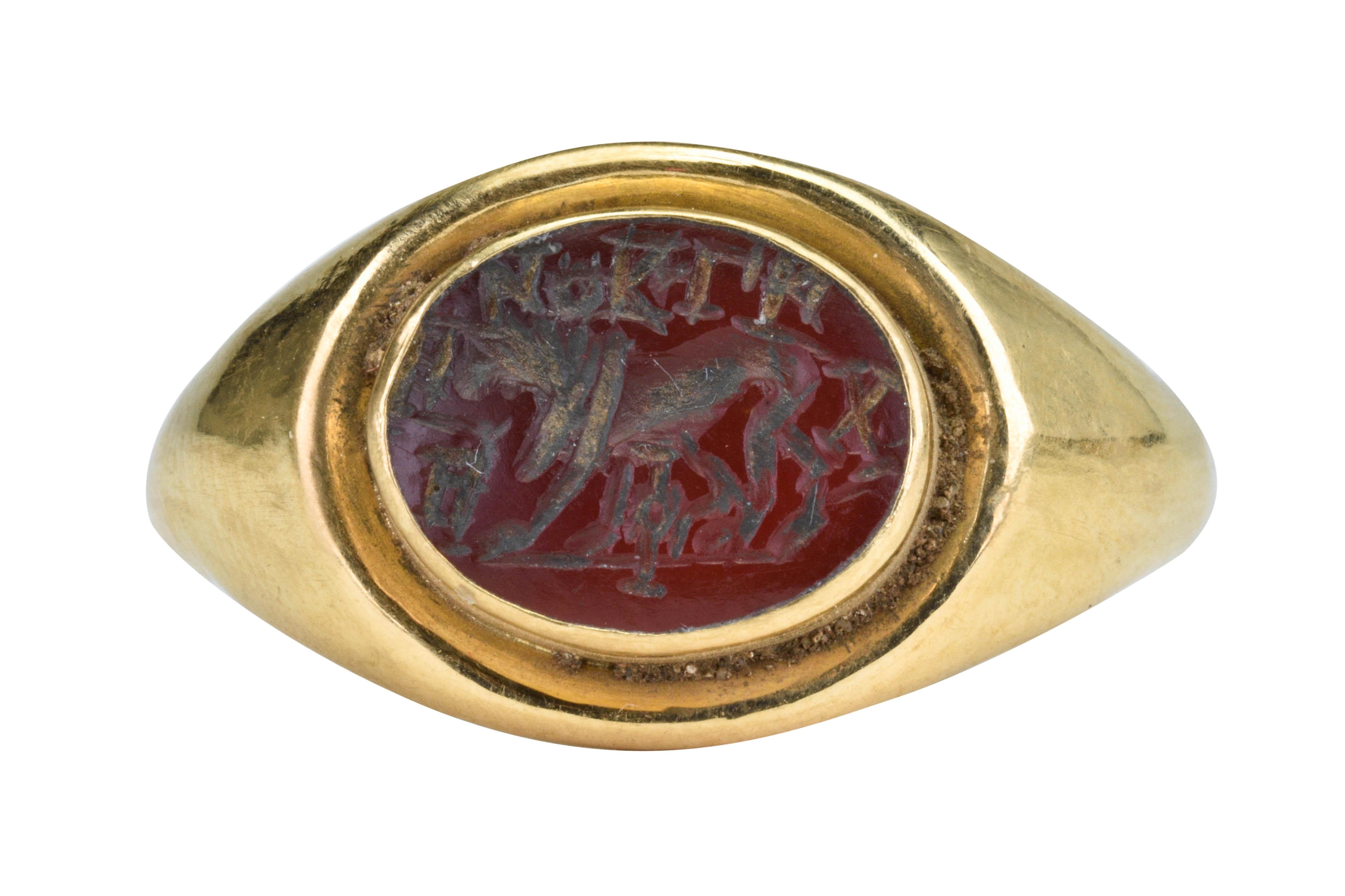Ancient Roman Gold Signet Ring with Lion and Script

Ca. 100-300 AD

An Ancient Roman gold finger ring composed of a carinated-section round hoop rising to an oval bezel containing a carnelian intaglio depicting a walking lion on a baseline. The