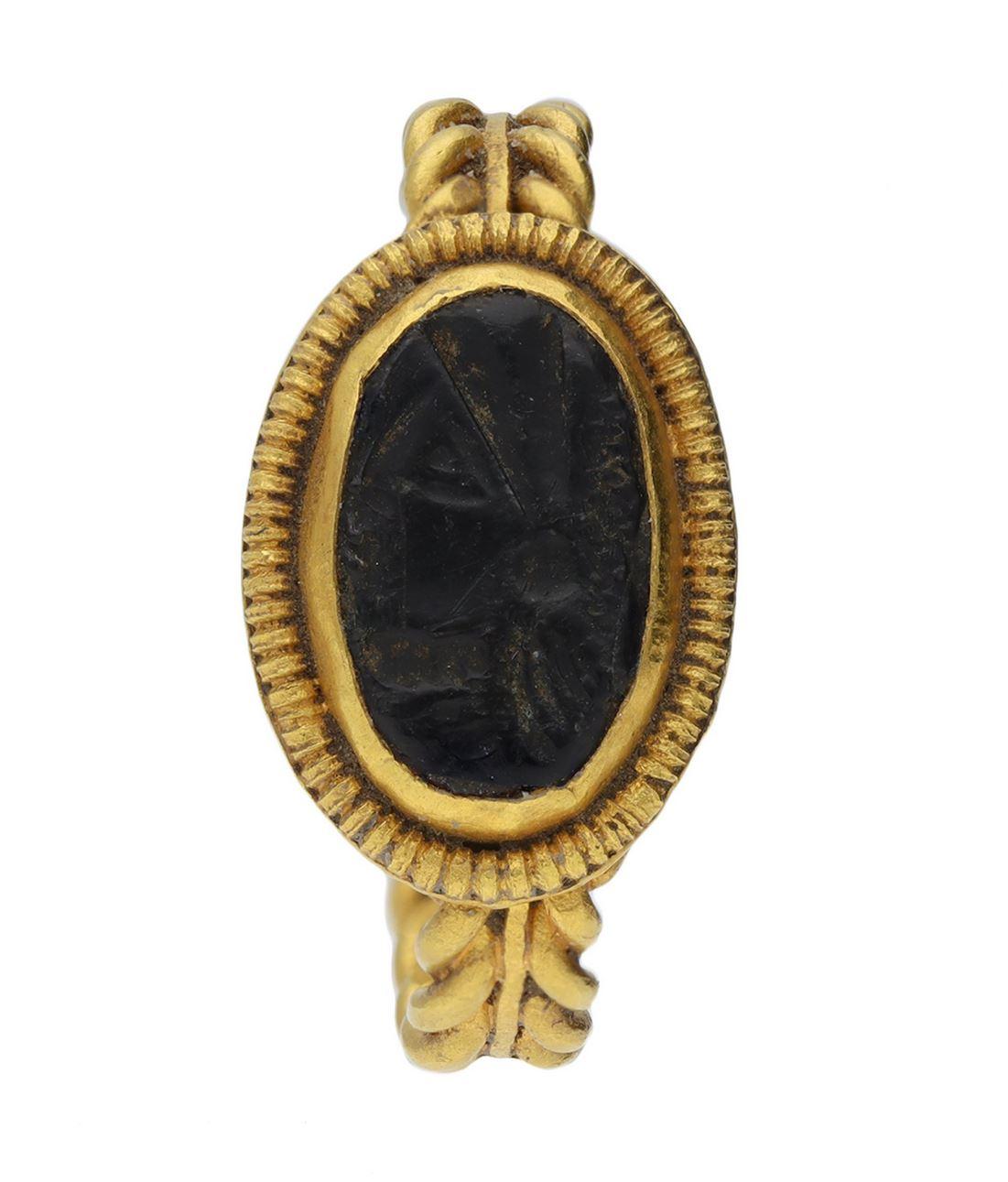 Ancient Roman intaglio ring. Set with an oval black glass intaglio engraved with a profile of a bust in a closed back Roman set setting, framed by a row of intricate semi-circular engravings and set on a twisted gold wirework shank with central flat