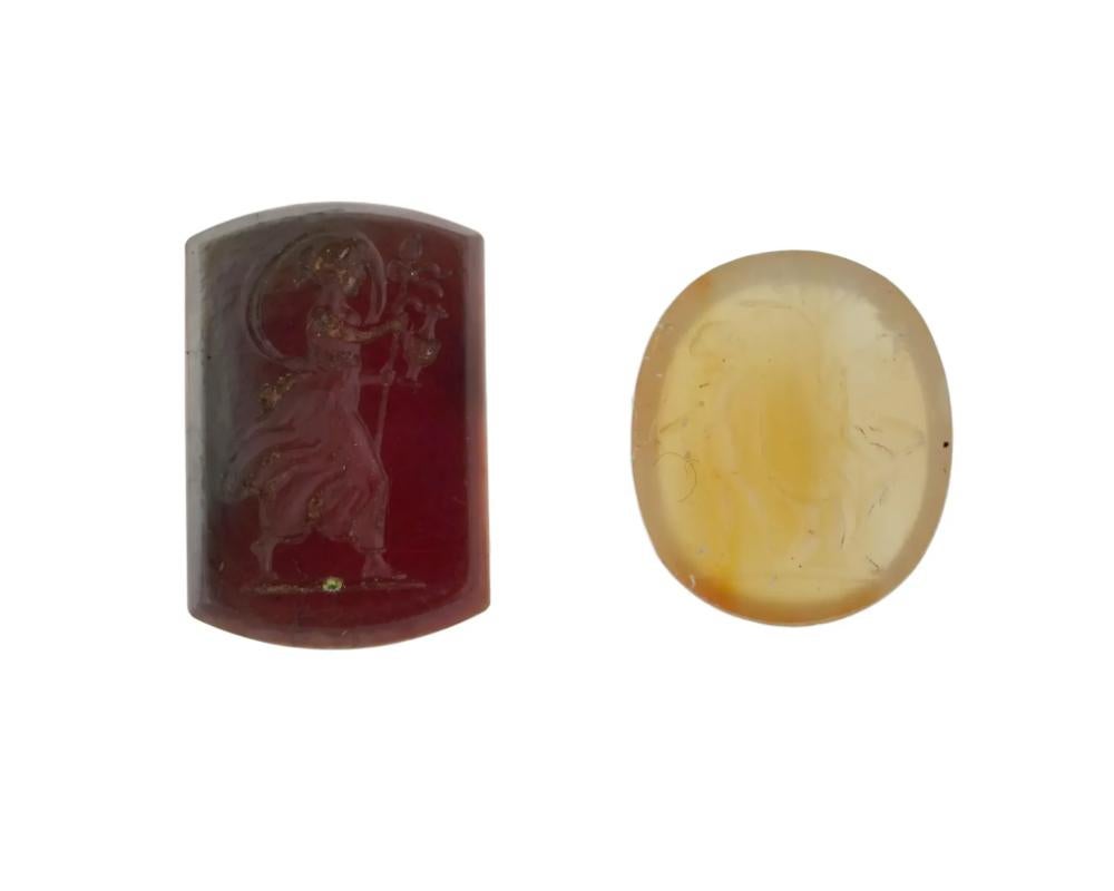 Un lotto di due antichi sigilli calcografici romani, realizzati con pietre semi preziose. Dal II al III secolo d.C. circa. La prima incisione, di forma rettangolare su una pietra marrone scuro, raffigura una ninfa che cammina con un bastone fiorito