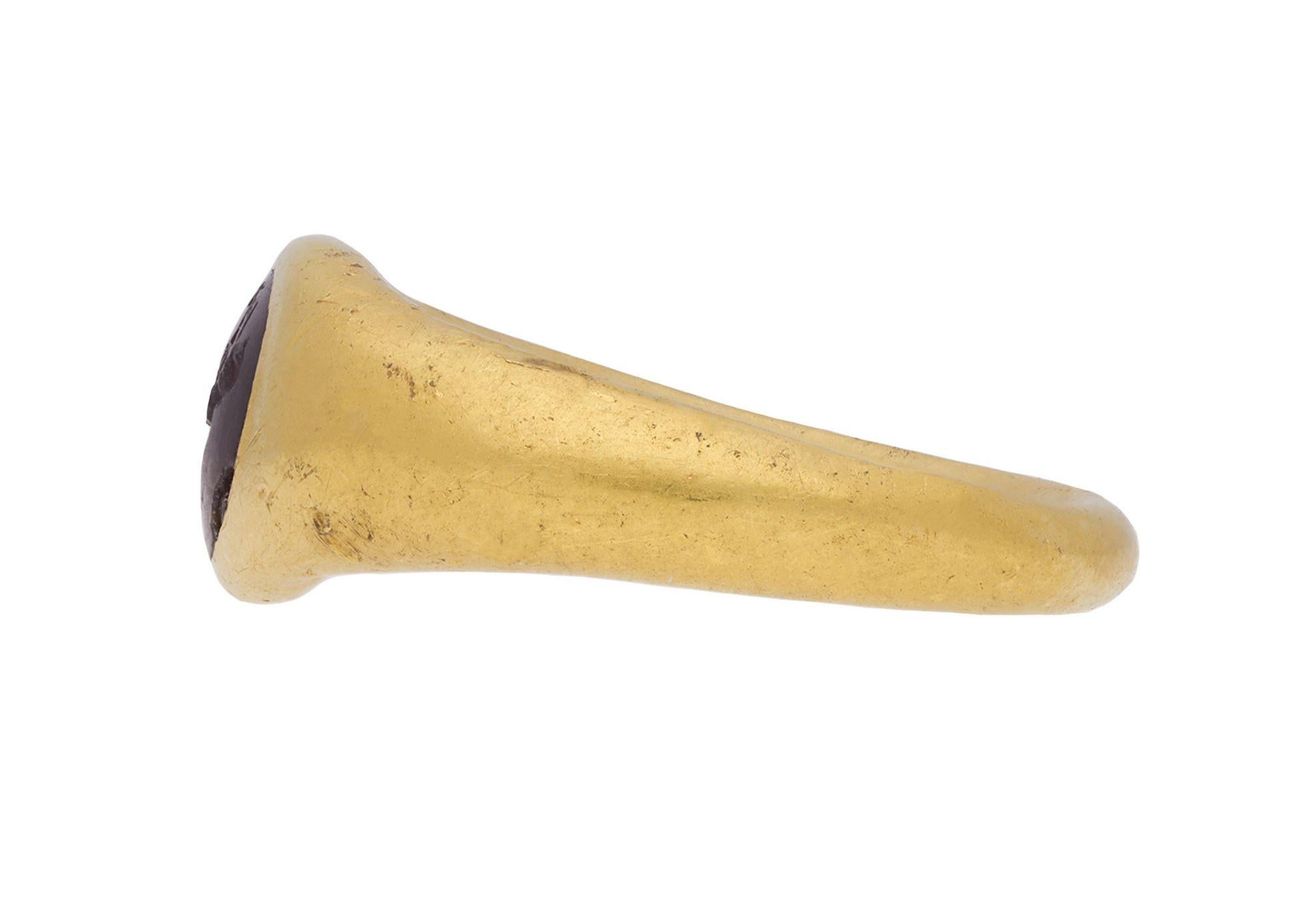 Ancient Roman Kneeling Athlete intaglio. Set to centre with an oval garnet intaglio in a closed back setting, engraved with a kneeling athlete holding a discus, leading to trumpeting shoulders and flowing through to a solid shank. Tested yellow