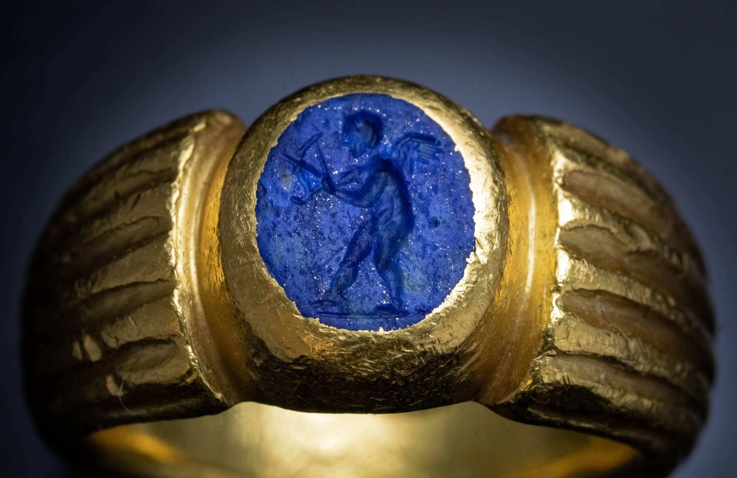 The Roman Empire, circa 2nd century A.D.  This heavy solid ring is cast in almost pure gold. The ring features a lapis lazuli intaglio finely engraved with a winged Eros (God of Love and Sexuality) armed with a bow.  The lapis intaglio is set in a