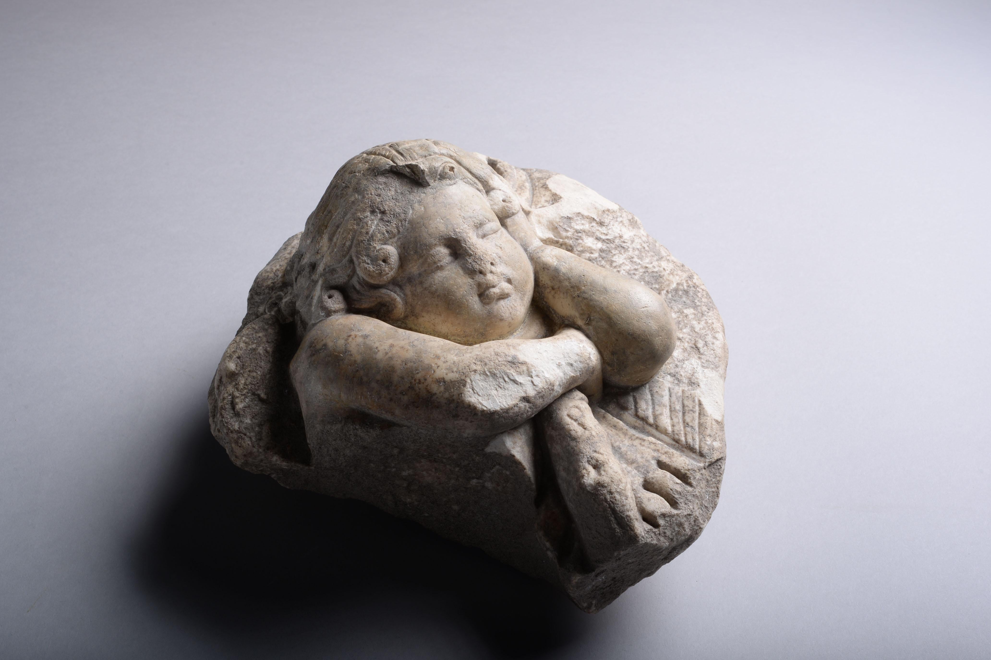 Roman marble figure of Eros, circa first-second century AD. 

With his right arm folded across his chest and his cheek resting on his left, his plump lips are pursed and his tussled hair tumbles from his head in long, loose locks. The knotted club