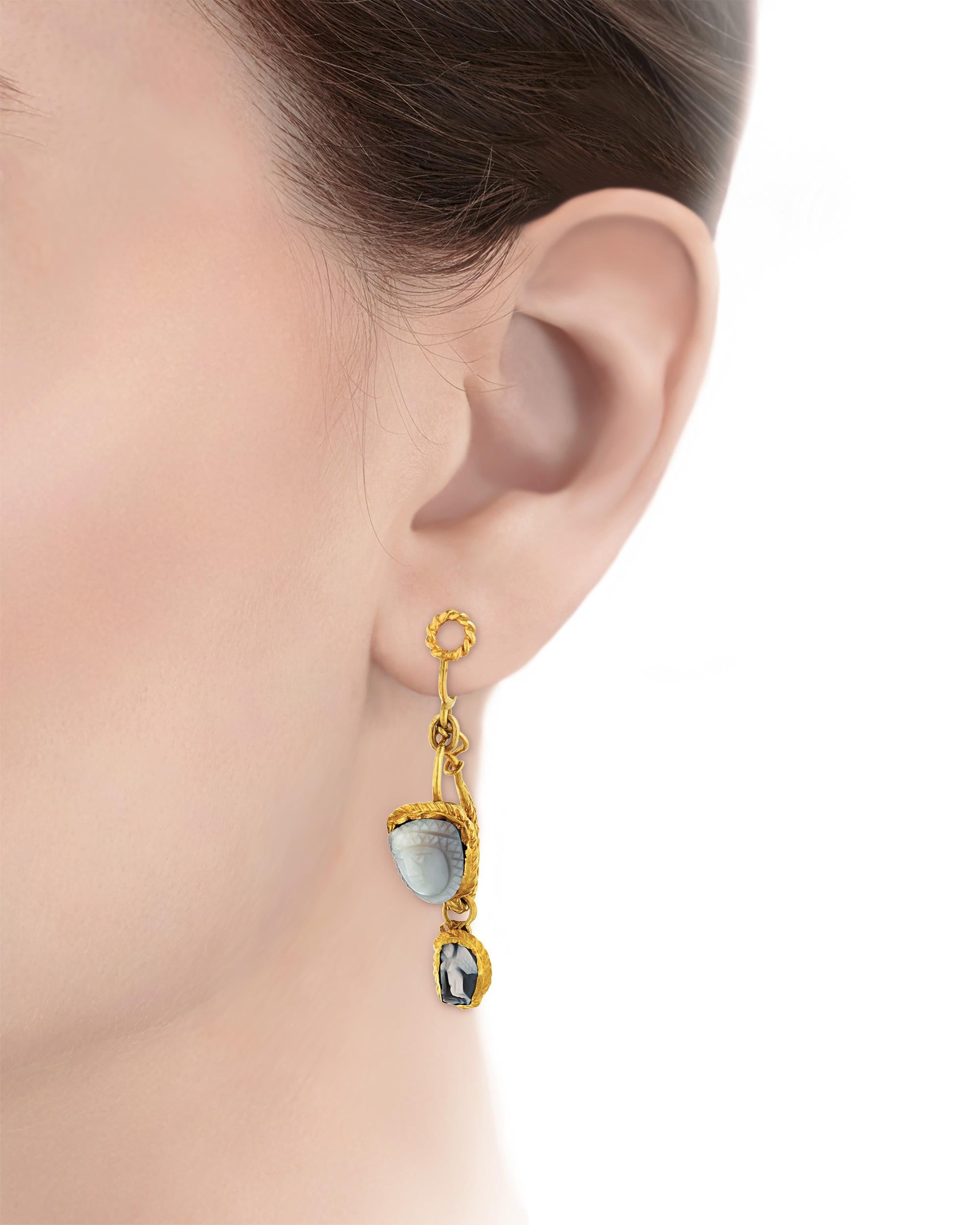 Displaying two carved Medusa gemstones over 1800 years old, these dangle earrings are exceptional examples of the ancient Roman intaglio technique. Paired with a 19th-century gold setting and accented by two additional Victorian cameos, these