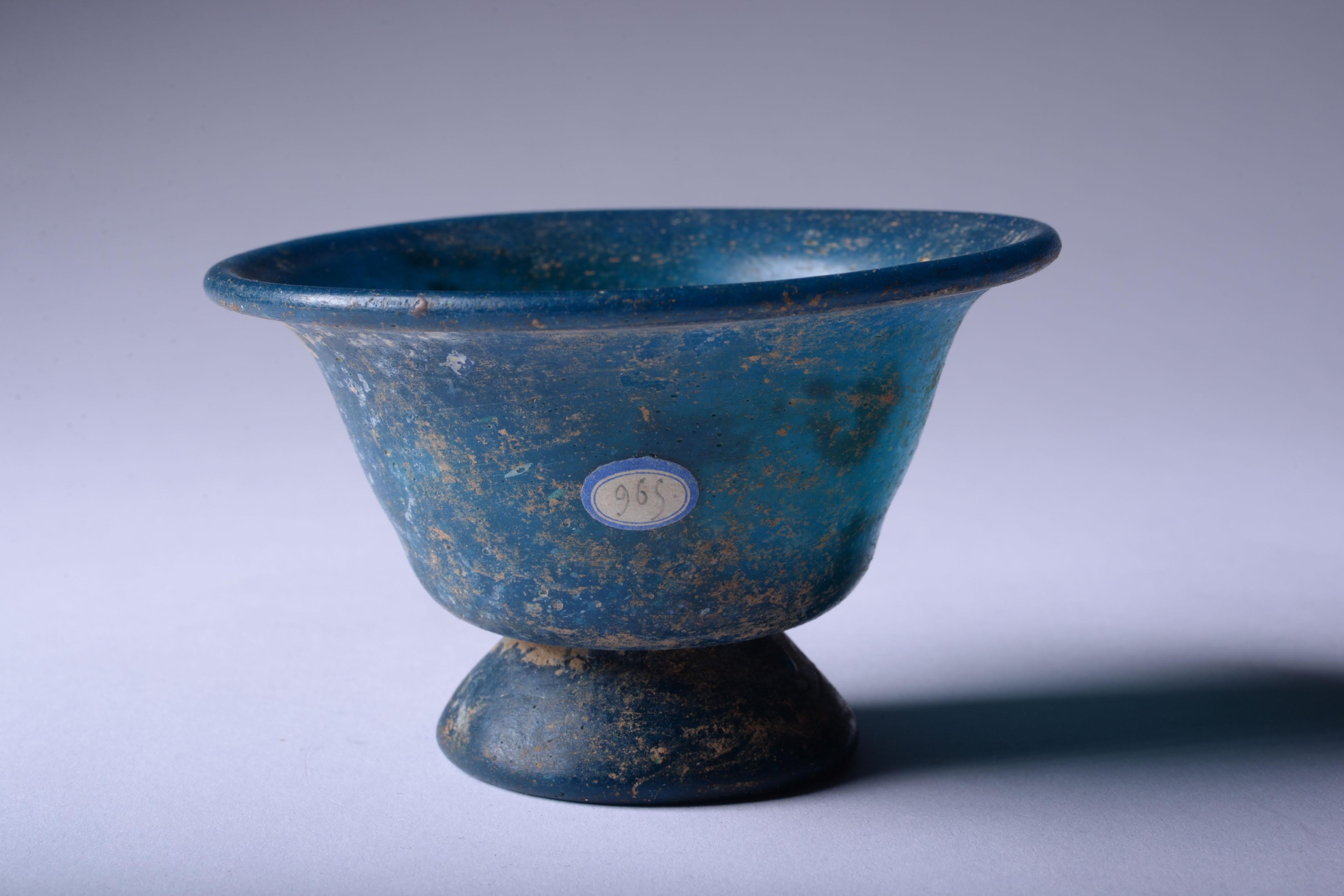 Turquoise glass cup 
Roman Empire, circa 3rd-4th century A.D. 
With old label reading ‘’965’’.

“Pliny relates that the art of glass-making [.] was actually discovered under the reign of Tiberius, and that the shop and tools of the artist were