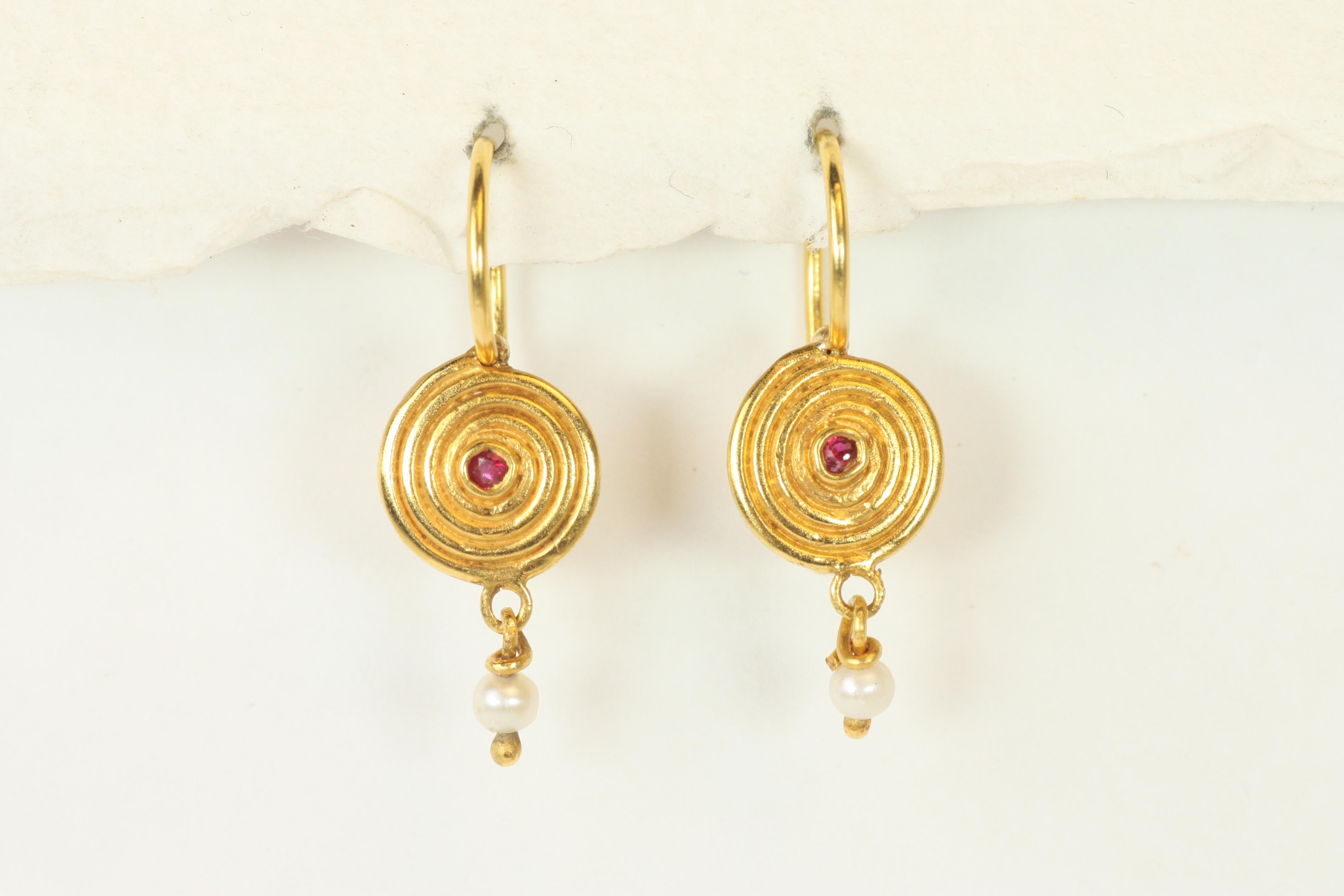 Questi orecchini Ruby Swirl combinano lo splendore dei rubini e delle perle con un iconico design artigianale. Realizzato in oro giallo 22 carati, il motivo vorticoso evoca un'eleganza senza tempo, mentre una perla luminosa pende delicatamente al di