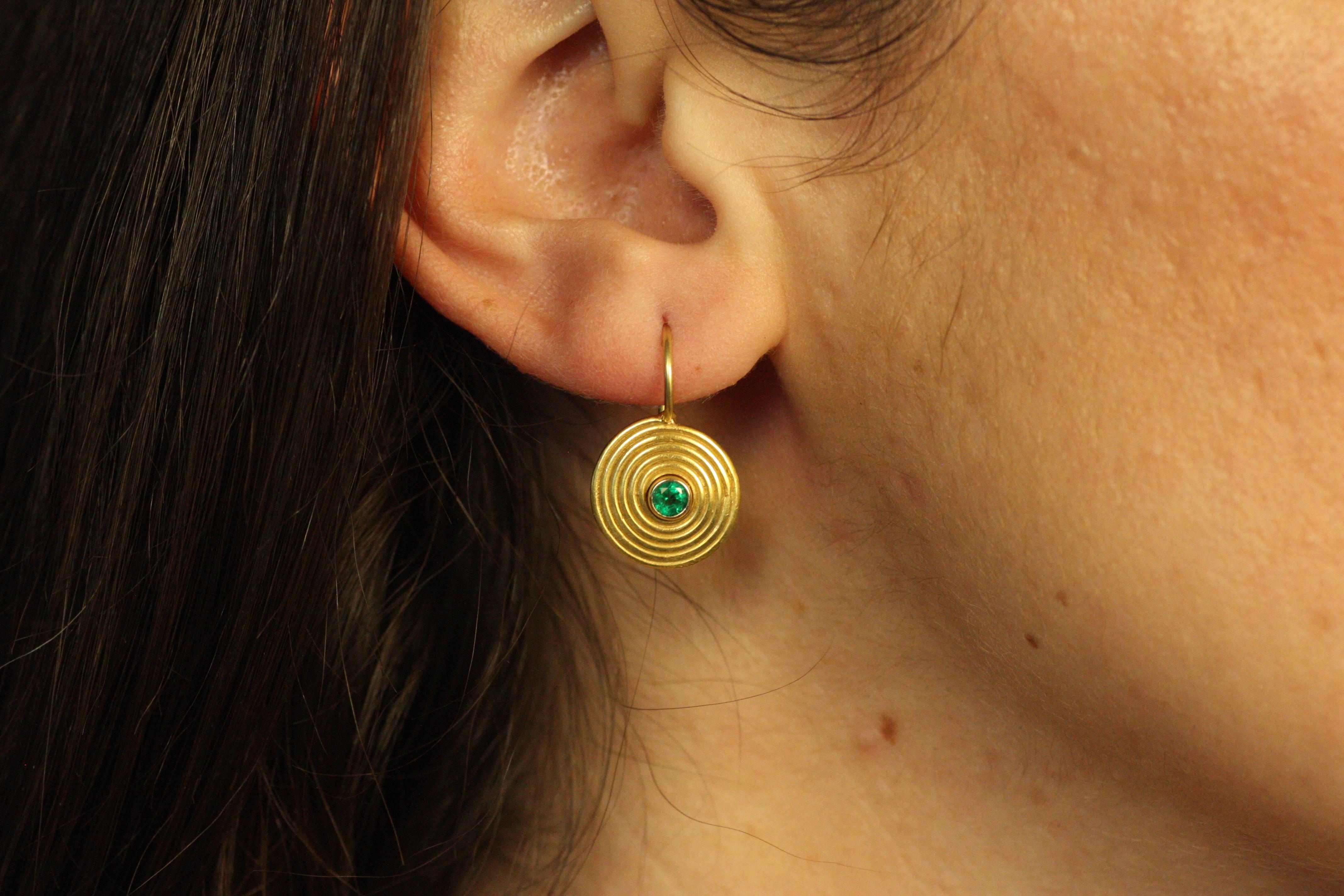 The Ancient Spiral Earrings are a timeless representation of intricate craftsmanship. Crafted in 22k yellow gold, these earrings feature a mesmerizing spiral design that radiate from a central emerald, bezel-set to highlight its vivid green color.
