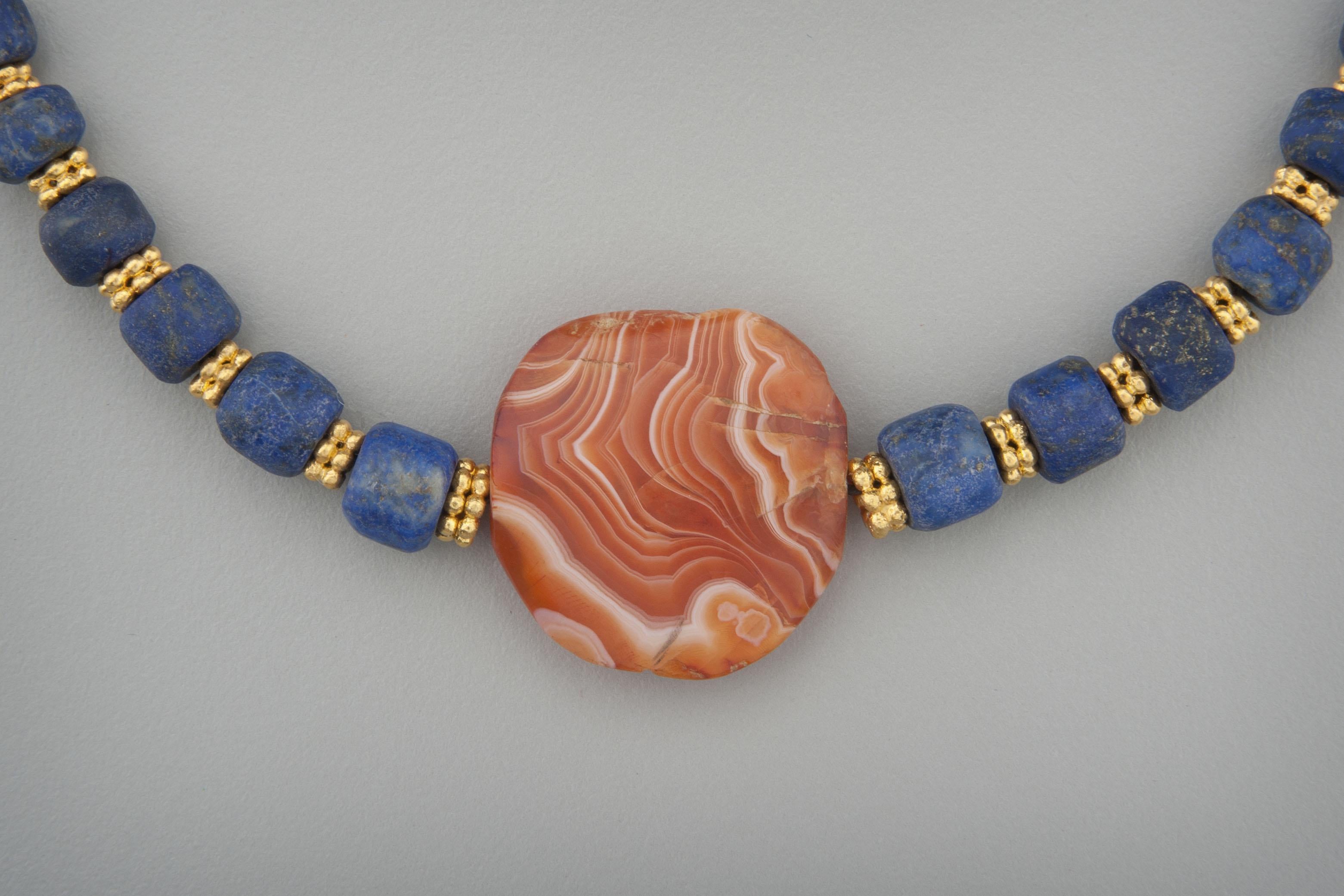 Thirty-five lapis lazuli beads spaced with 24k gold double layer granulated ring beads with a tabular sardonyx bead at the center.  Gold beading tips and a hook and eye clasp complete the necklace. The sardonyx is carnelian veined with transparent