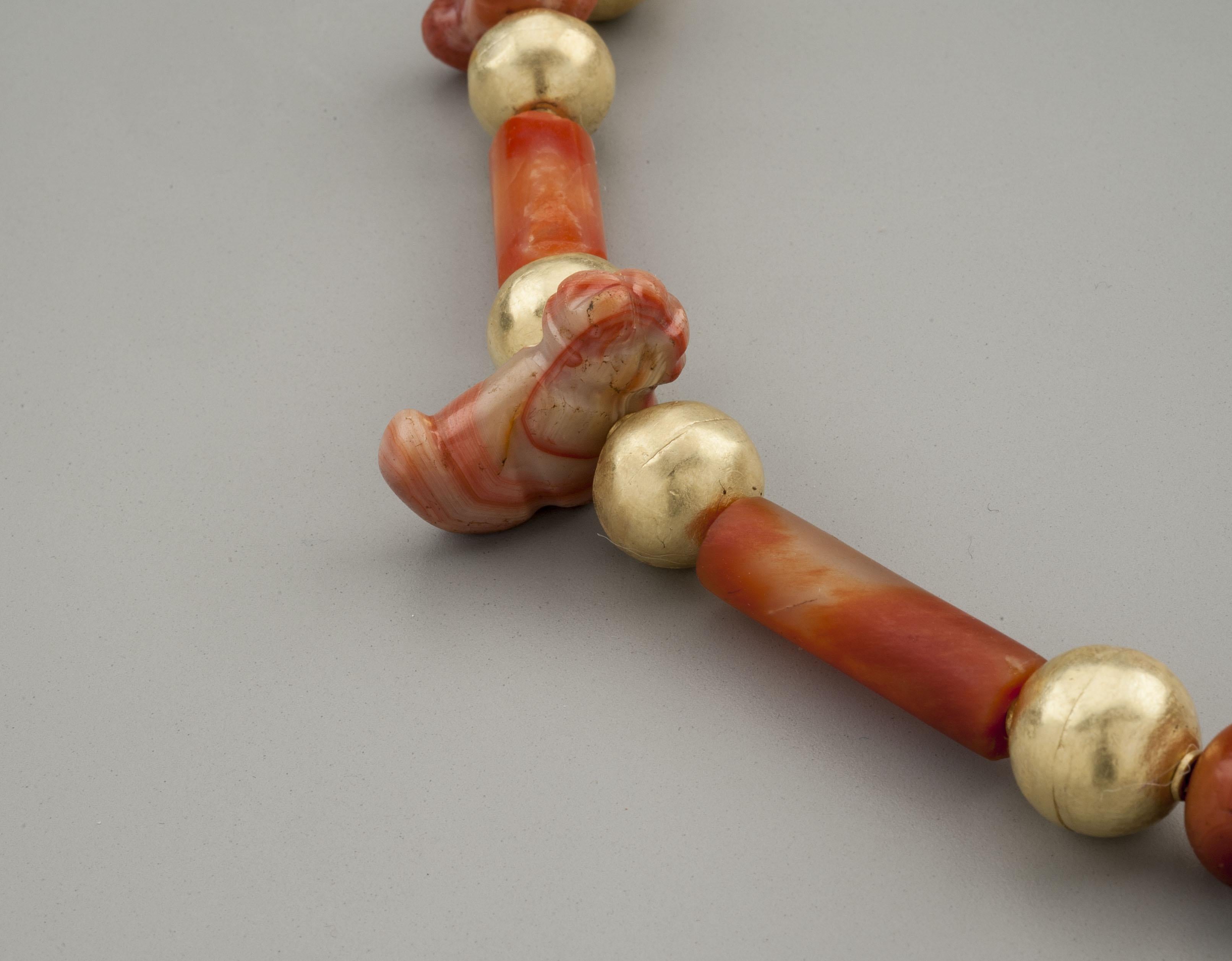 Five carnelian amulets in the form of larva or grubs, inter-spaced with fourteen carnelian beads, both round and cylindrical, alternating with sixteen large round collared spherical gold beads. Two more spheres form beading tips and there is an