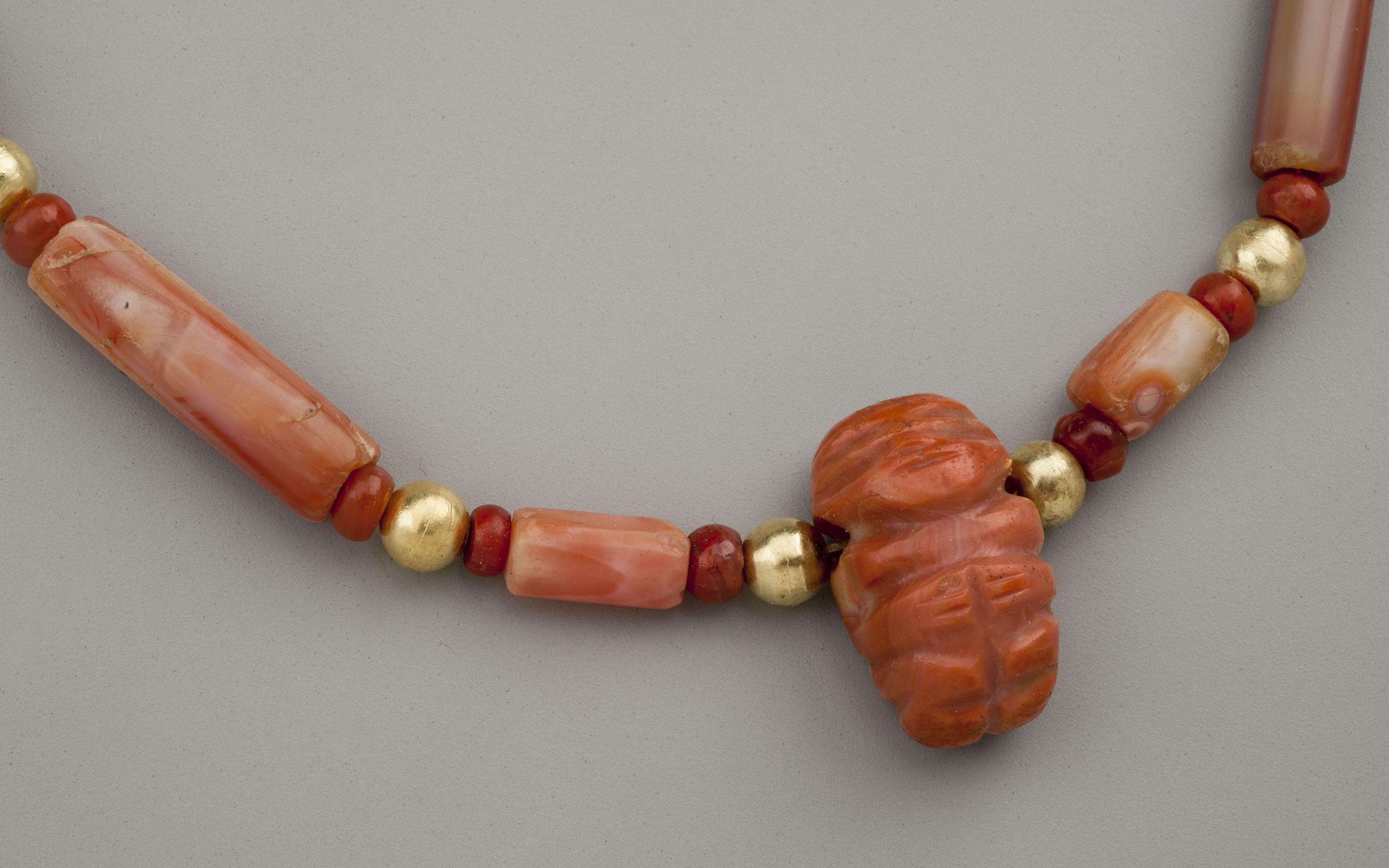 Thirty-six carnelian beads, twelve of cylindrical form and twenty-four round beads and twelve round gold beads and a carnelian effigy of a man (presumably a chief) pendant. The stone pieces are said to be from the Tairona people of Colombia, South