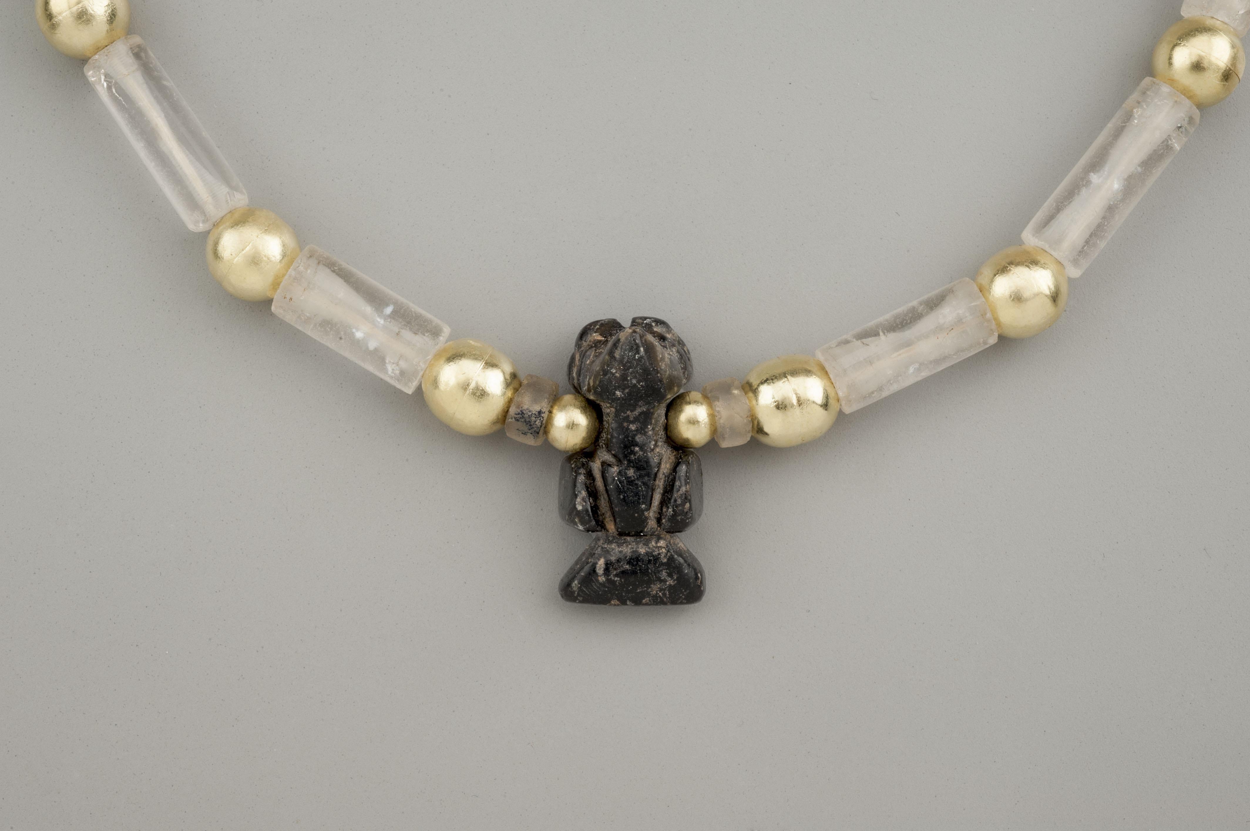 Twenty-two rock crystal cylinder beads alternating with round gold beads with a black stone eagle pendant. The stone beads and pendant are said to be from the Tairona people of Colombia, South America. They have been made entirely without the use of