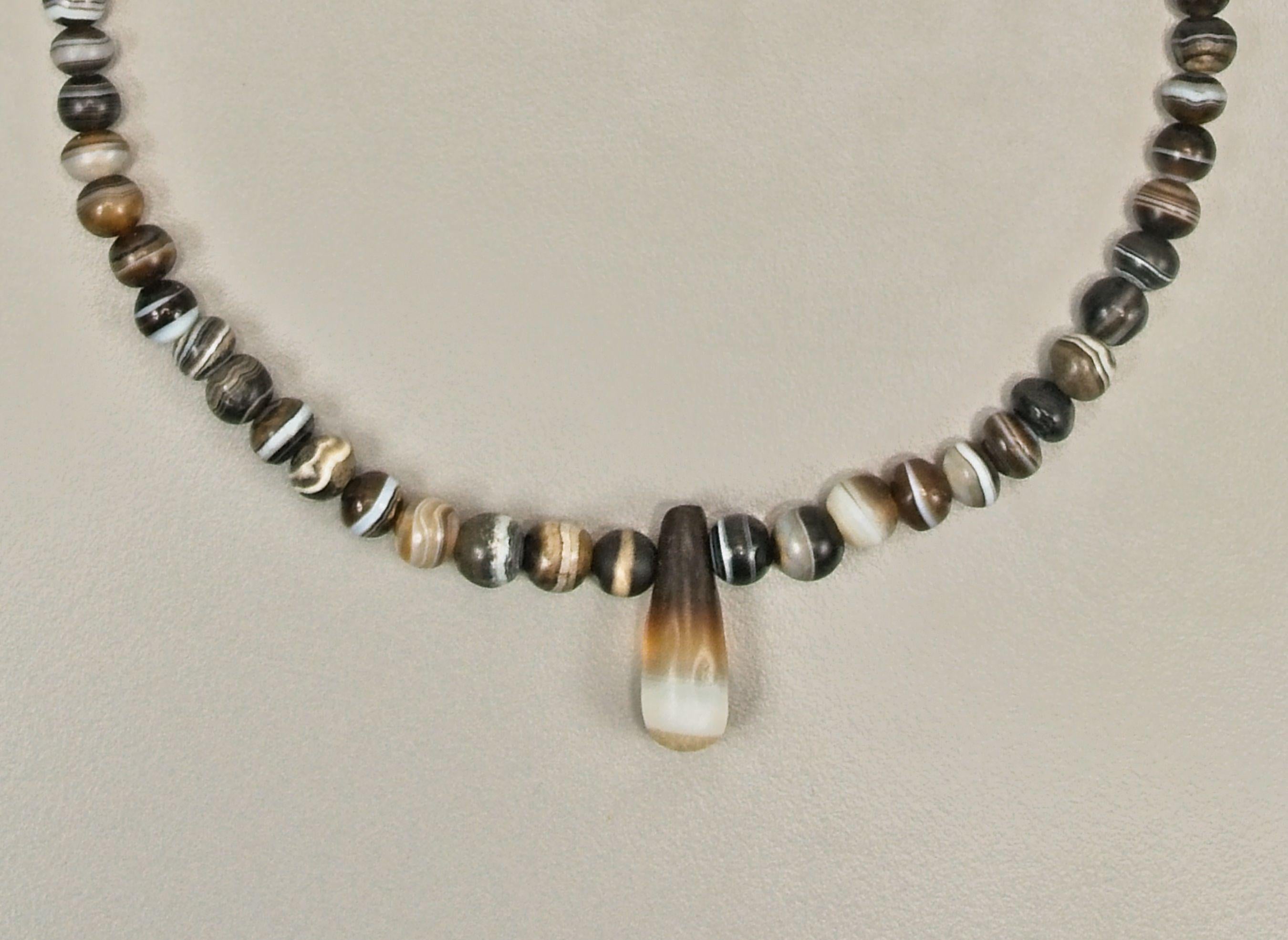 Seventy-four round agate beads with a teardrop shaped pendant bead at the center. The pendant is 2.82 cm in height, 1 cm in width at the bottom. The drill hole is 4 mm from the top and is 2.3 mm in diameter. The beads graduate in size from the front