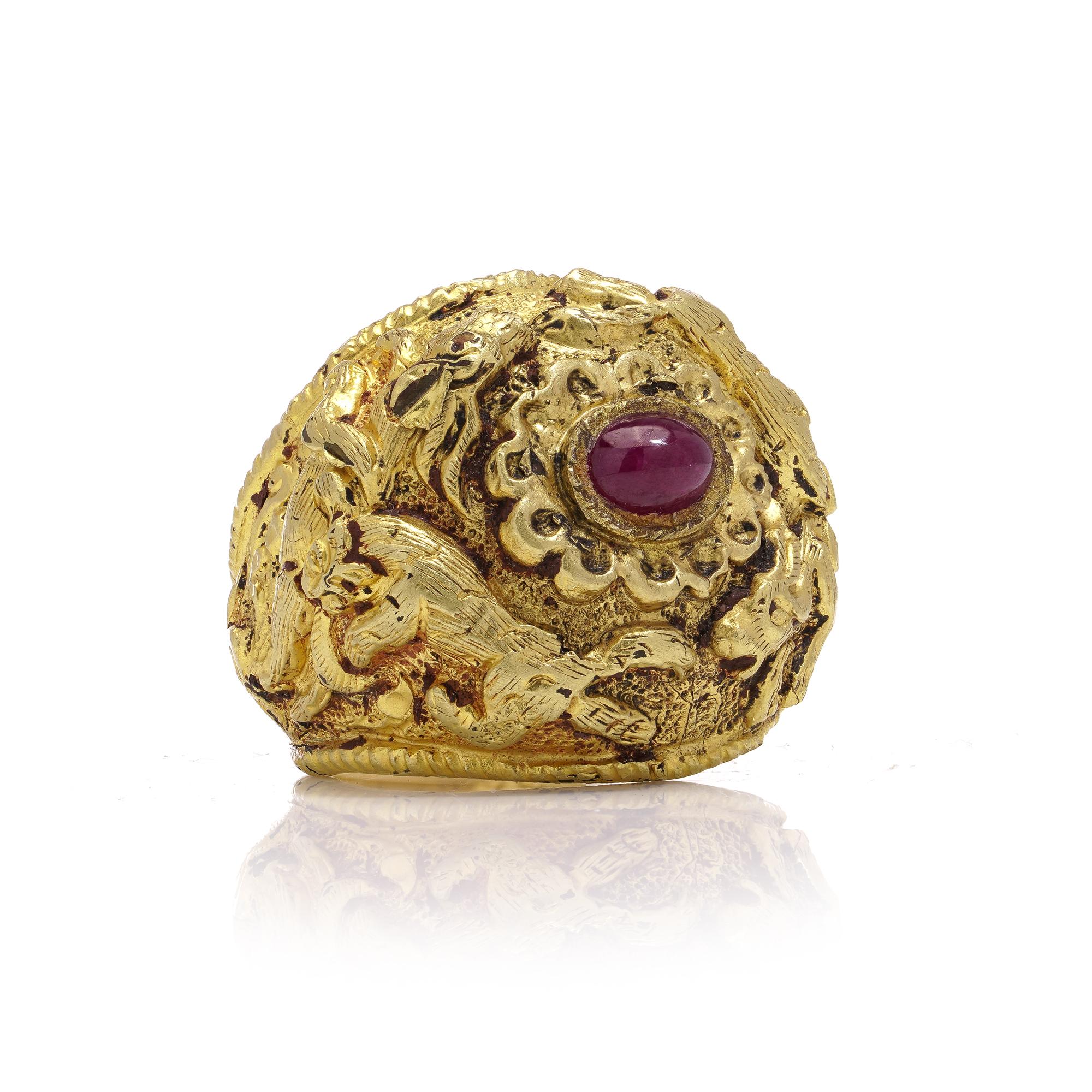 A 20kt yellow gold ring from ancient Thailand features a central ruby surrounded by depictions of hunting scenes. The scenes include leopards hunting rabbits and oxen. X-ray analysis revealed that the ring is made of 20kt gold with a blend of