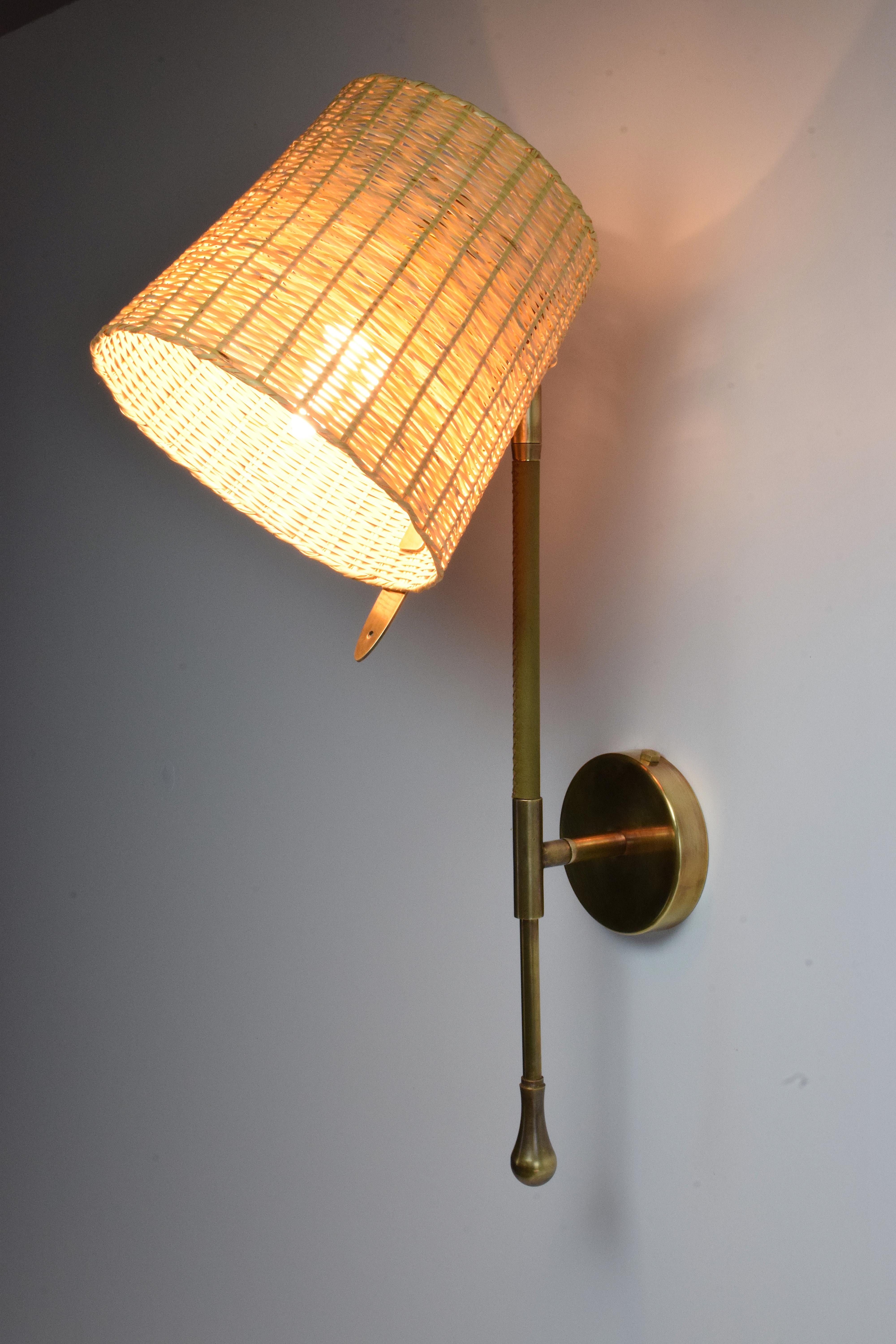 Contemporary handcrafted articulating wall lamp fixture or sconce, composed of a gold polished brass structure adorned with a  sheathed leather detail hand-sewn by artisan saddle workers, a handwoven wicker shade of rare craftsmanship with 90°