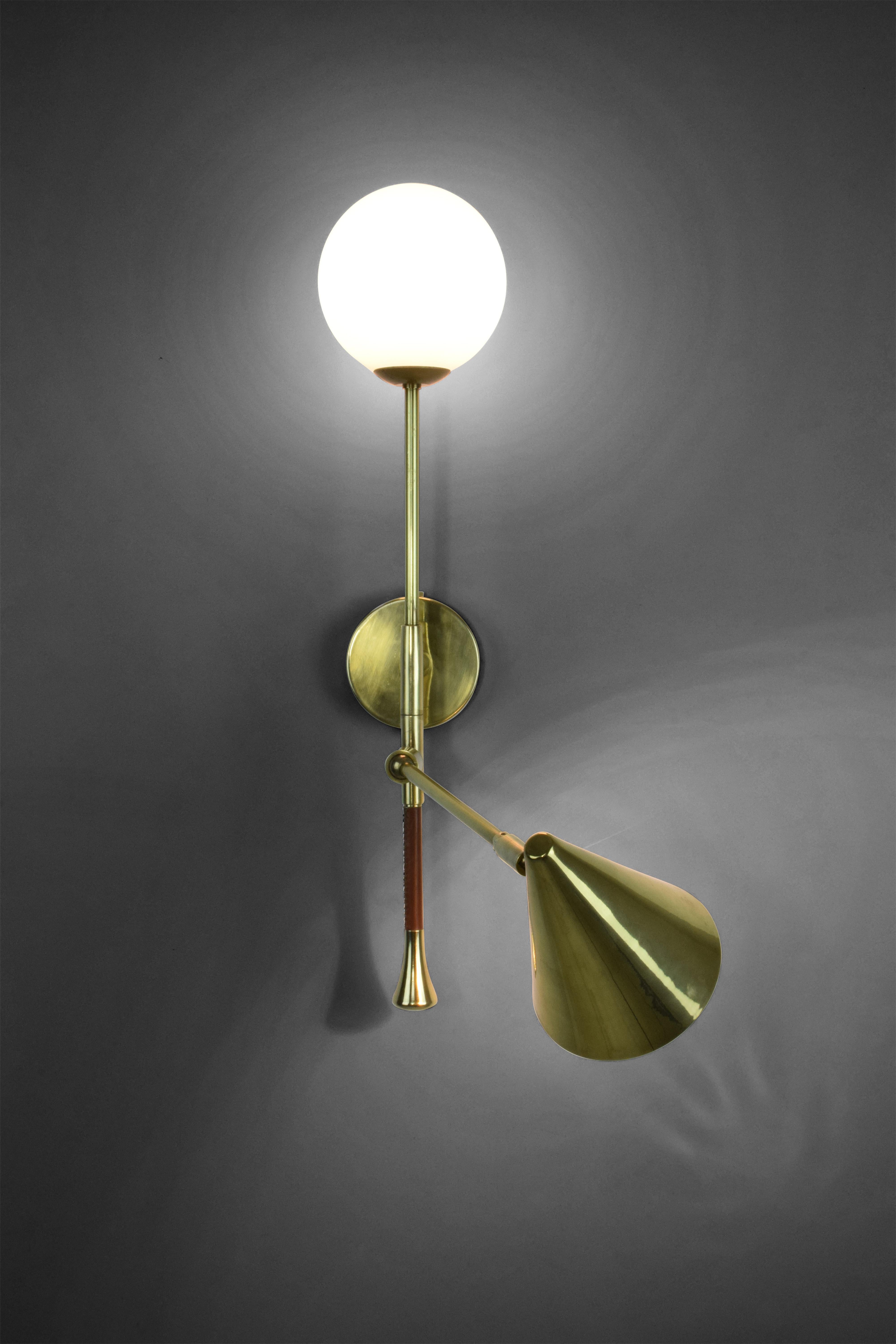 The DE.LIGHT is a solid brass double wall light with a leather sheathed stem detail. The main structure tops an opal glass di user or a cylinder fabric shade and the directional stem features a conic shade mounted with a moveable joint. Perfect as a